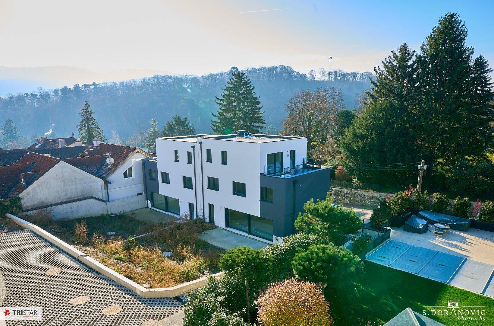 Neubau mit moderner Architektur und Flachdach, eingebettet in eine grüne Hügellandschaft.