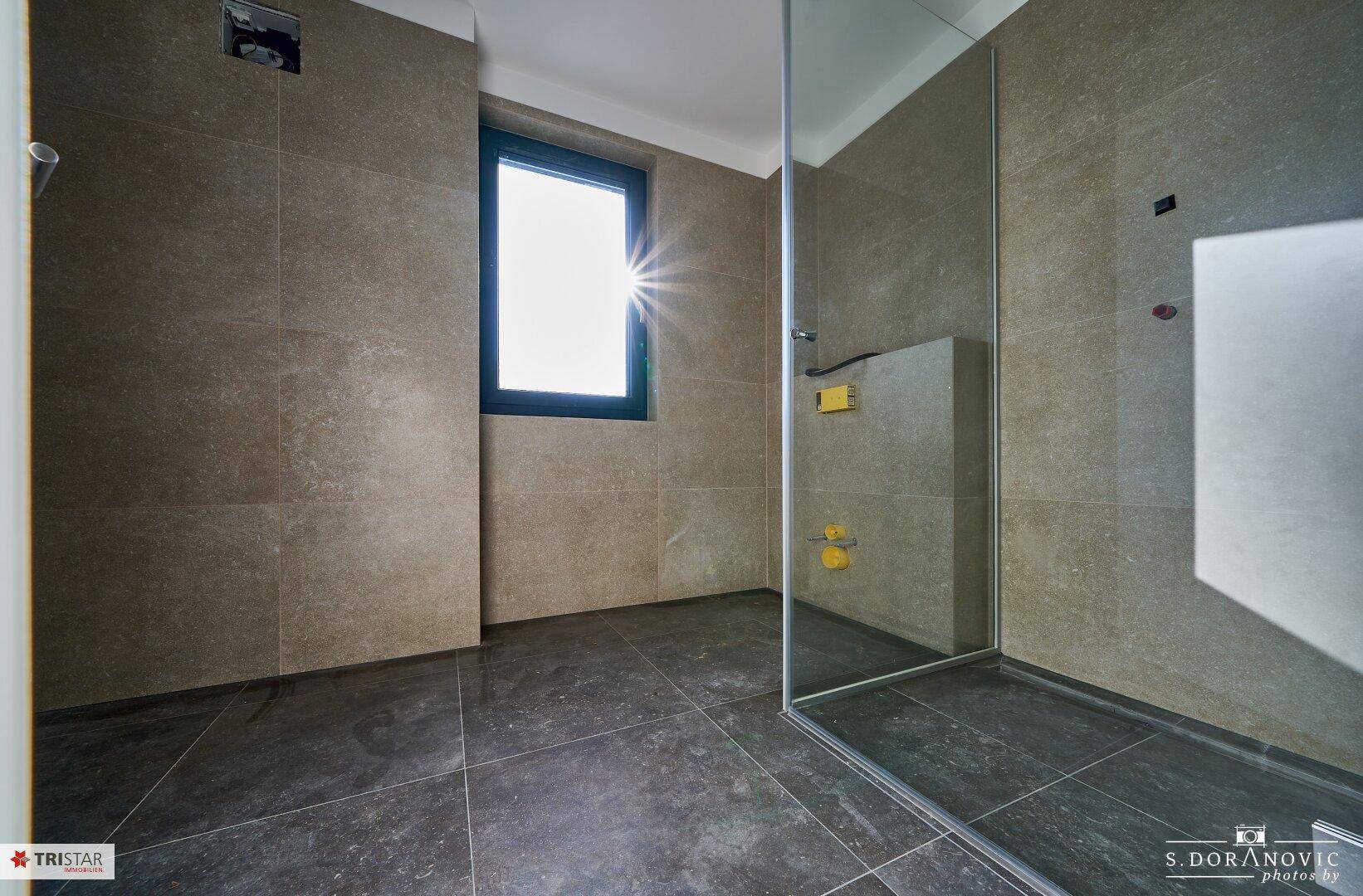 Modernes Badezimmer mit großen grauen Fliesen und einer begehbaren Dusche, bereit für die Installation.