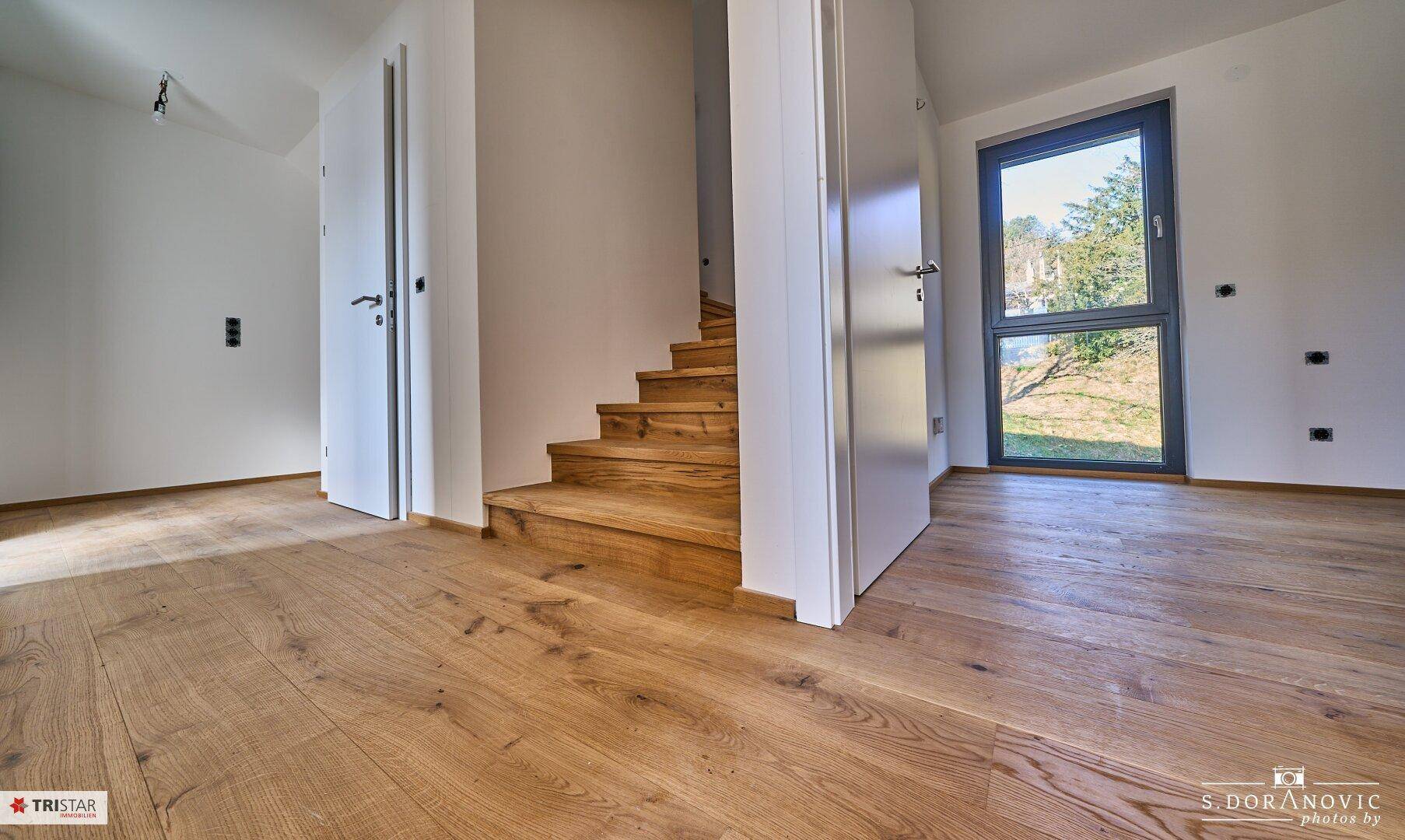 Heller Eingangsbereich mit Holzboden und offener Holztreppe, die in die oberen Etagen führt.