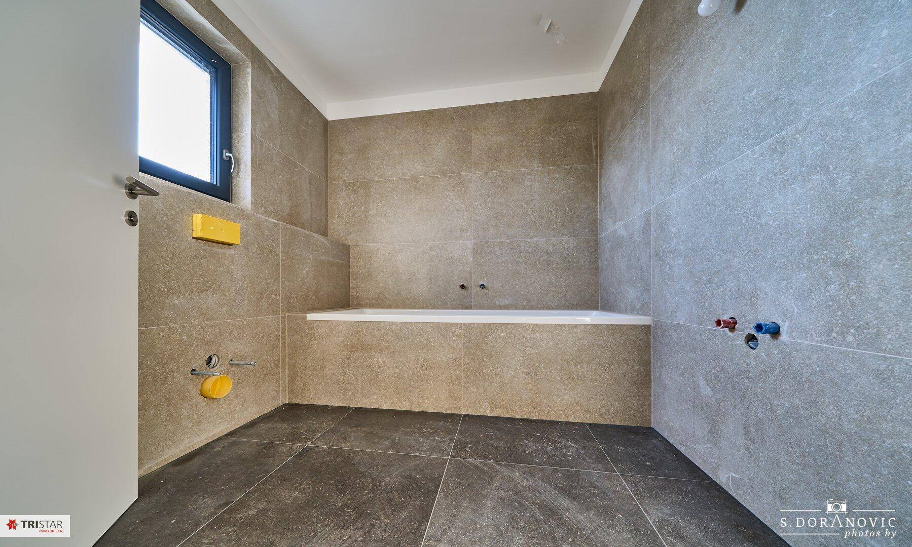 Modernes Badezimmer mit grauen Fliesen und einer eingebauten Badewanne, bereit für die Endmontage.