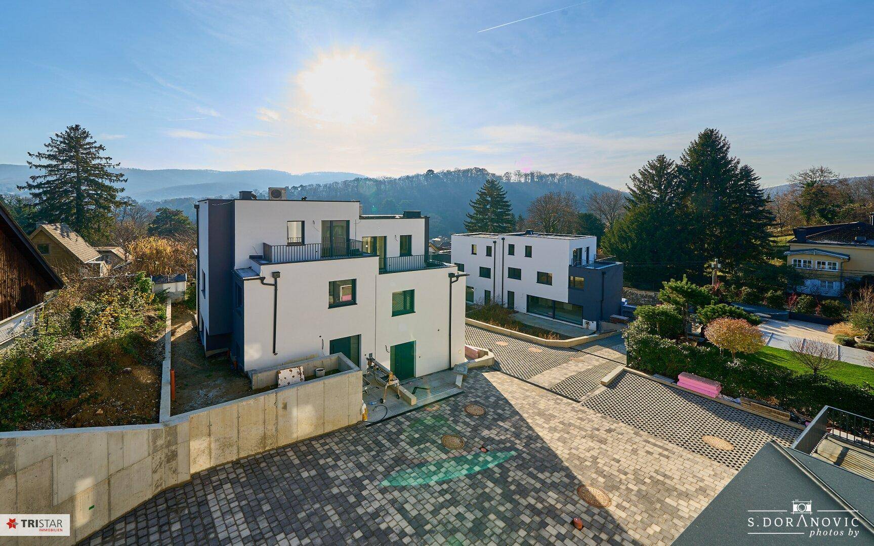 Zwei moderne Neubauten mit weißer und grauer Fassade, umgeben von Natur und mit Parkplätzen.
