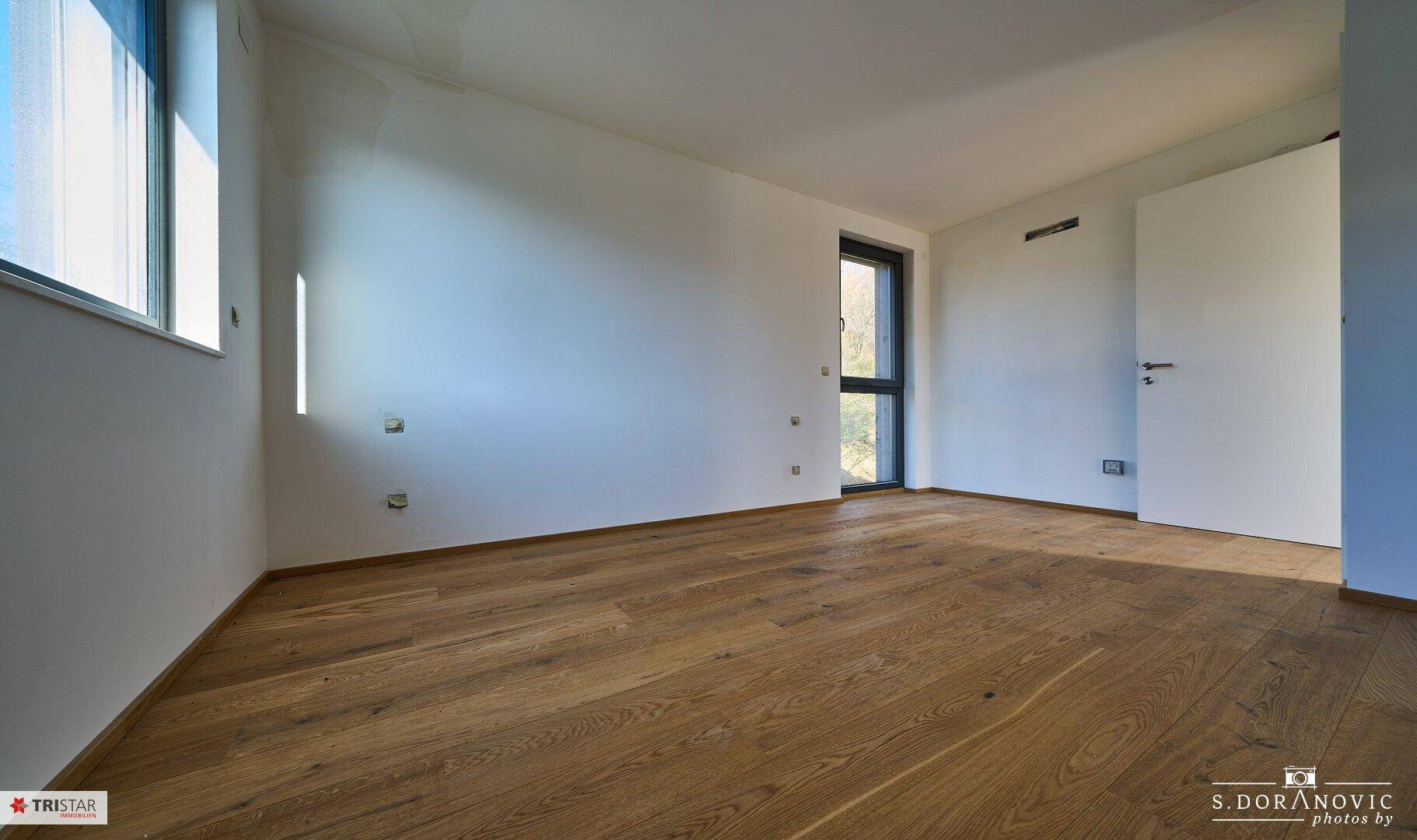 Helles Schlafzimmer mit Holzboden und einem Fenster, das viel Tageslicht spendet.