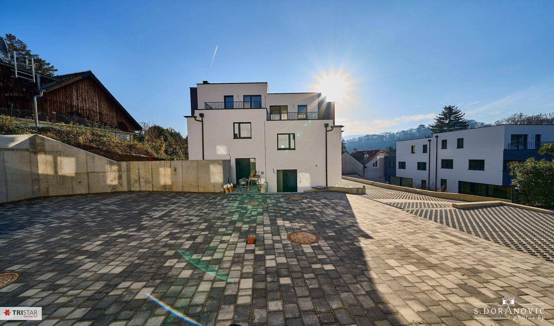 Rückansicht der modernen Wohnanlage mit großzügigen Parkflächen und sonniger Ausrichtung.