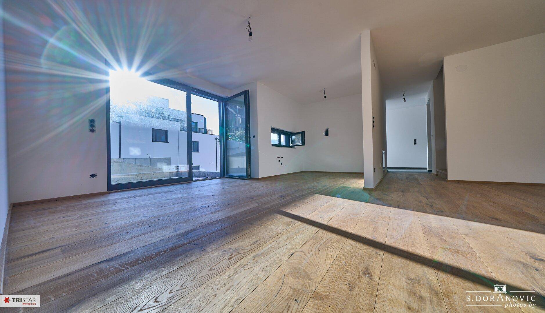 Heller Wohnraum mit Holzboden und Zugang zu einem Außenbereich, viel Sonnenlicht.