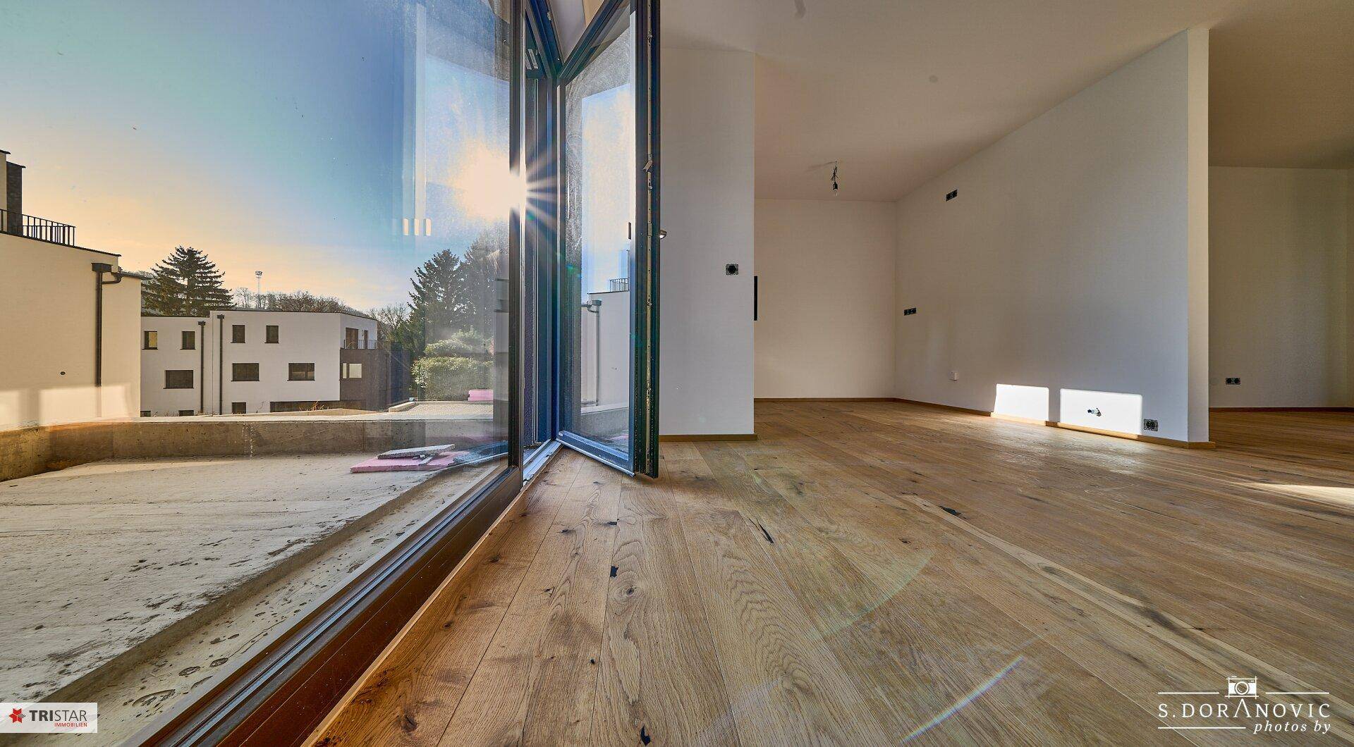Heller Wohnraum mit Holzboden und Zugang zu einem Außenbereich, viel Sonnenlicht.