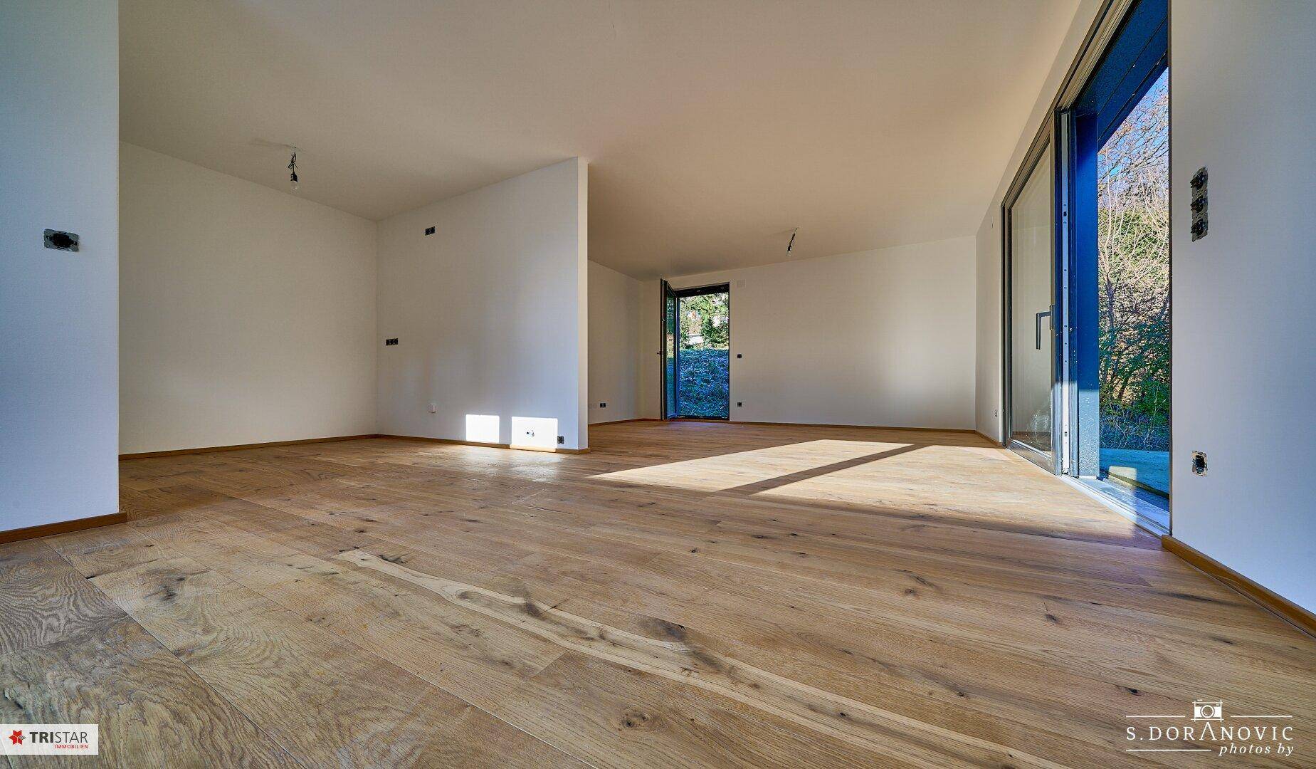Geräumiger Wohnbereich mit Holzboden und Zugang zum Garten, viel Tageslicht.