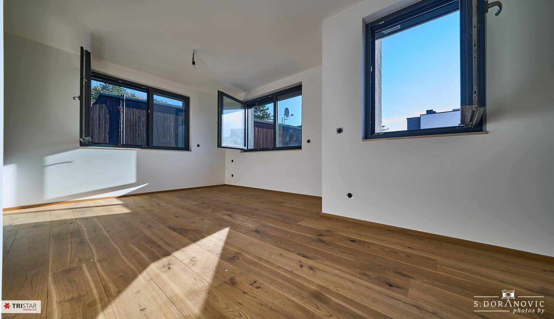 Helles Schlafzimmer mit Holzboden und mehreren Fenstern, die einen weiten Blick bieten.