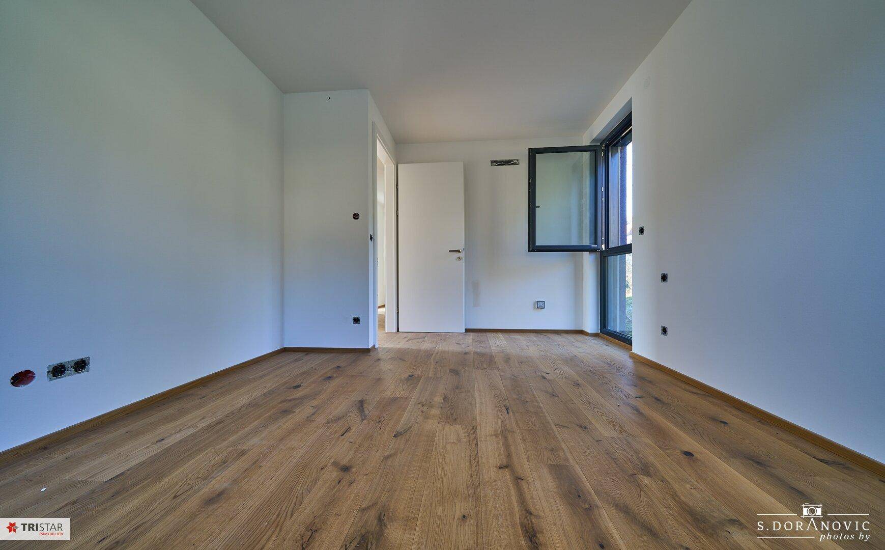 Helles Schlafzimmer mit Holzboden und einem Fenster, das viel Tageslicht spendet.