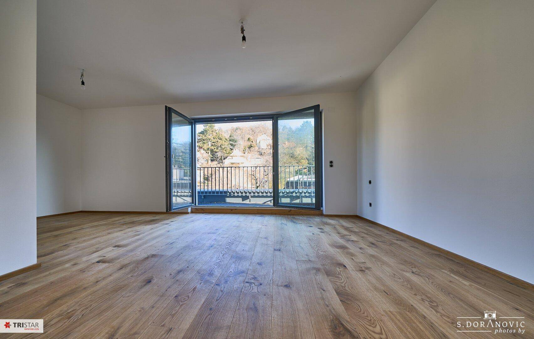 Helles Schlafzimmer mit Holzboden und großen Fenstern mit Zugang zum Balkon.