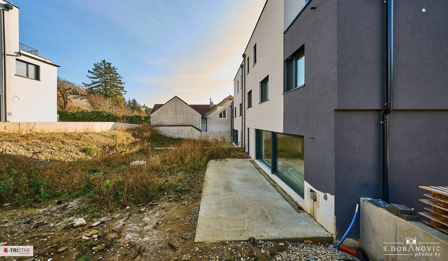 Moderne Gebäudeseite mit grauer und weißer Fassade, angrenzend an eine unbebaute Fläche.