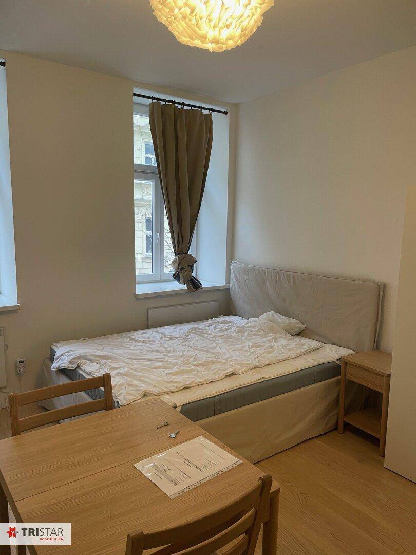 Heller Wohnraum mit komfortablem Bett und kleinem Esstisch, funktional eingerichtet und gut erhalten.