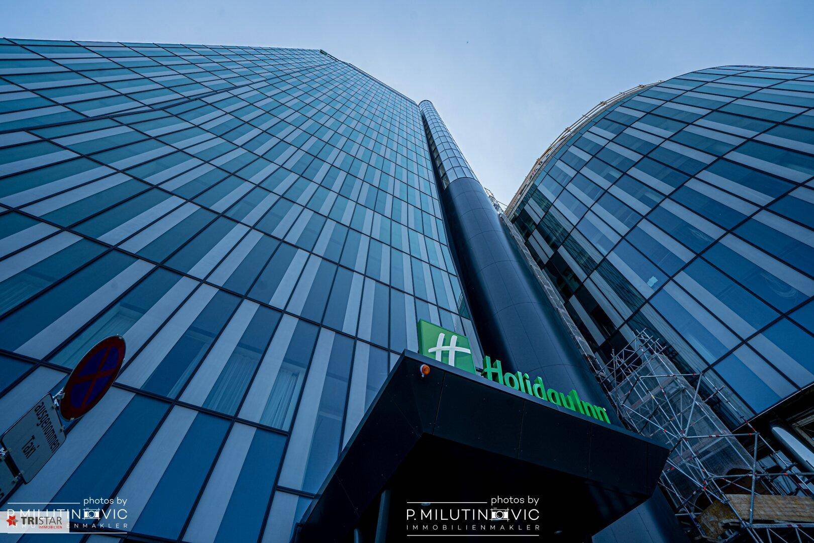 Modernes Hochhaus mit Glasfassade und dem Holiday Inn Logo unter blauem Himmel.