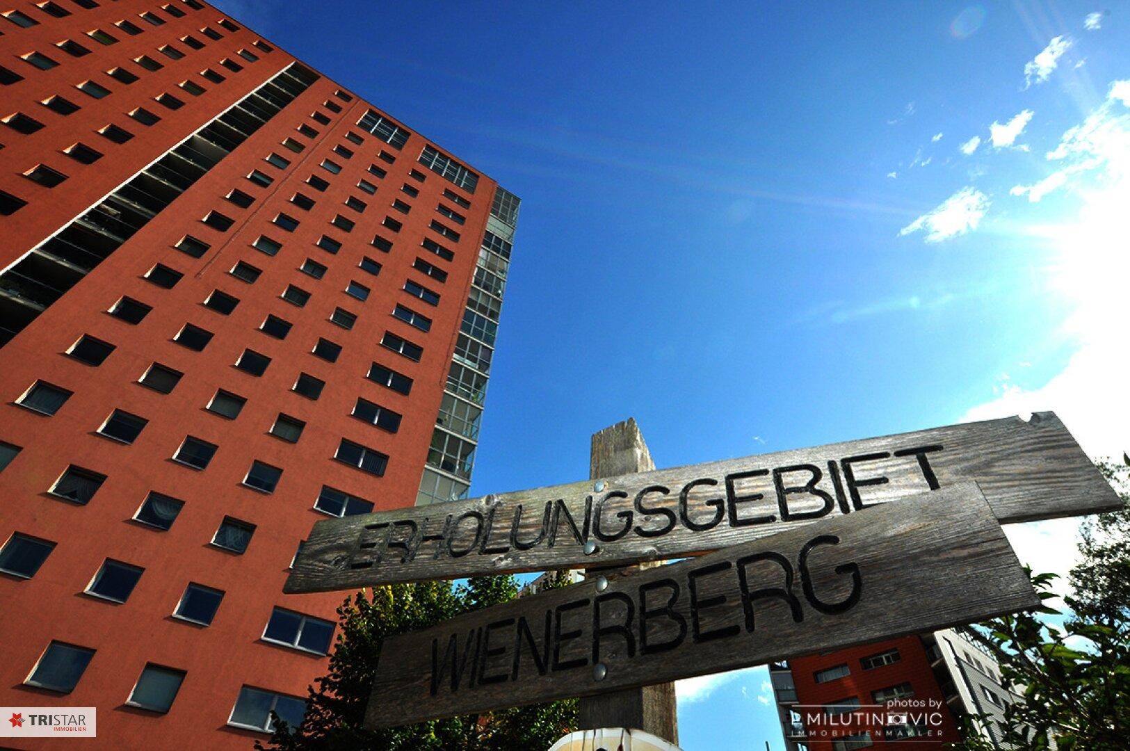 Hohes Wohngebäude mit Blick auf das Erholungsgebiet Wienerberg unter blauem Himmel.