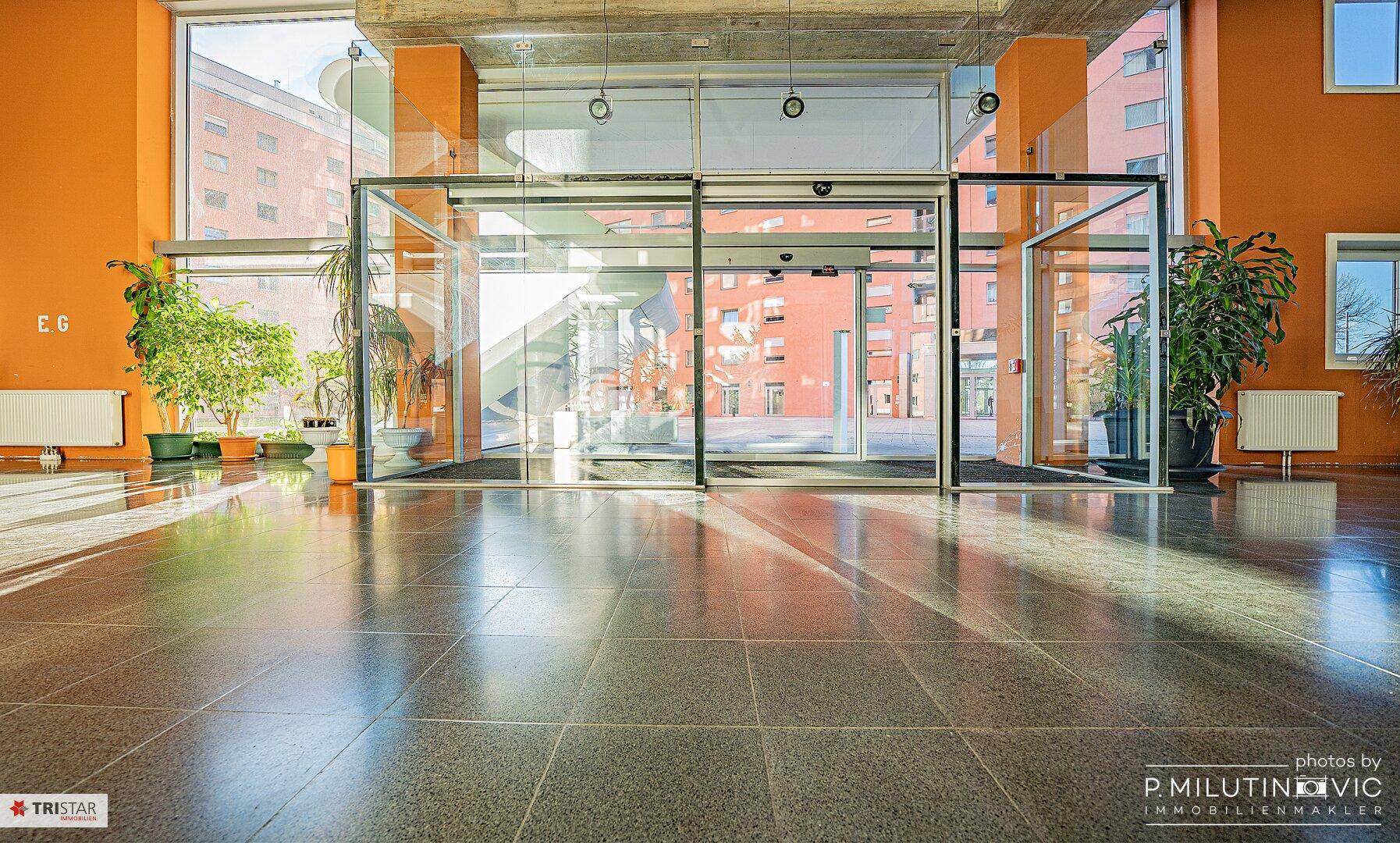 Heller Eingangsbereich mit Glasfront, automatischen Türen und glänzendem Fliesenboden.
