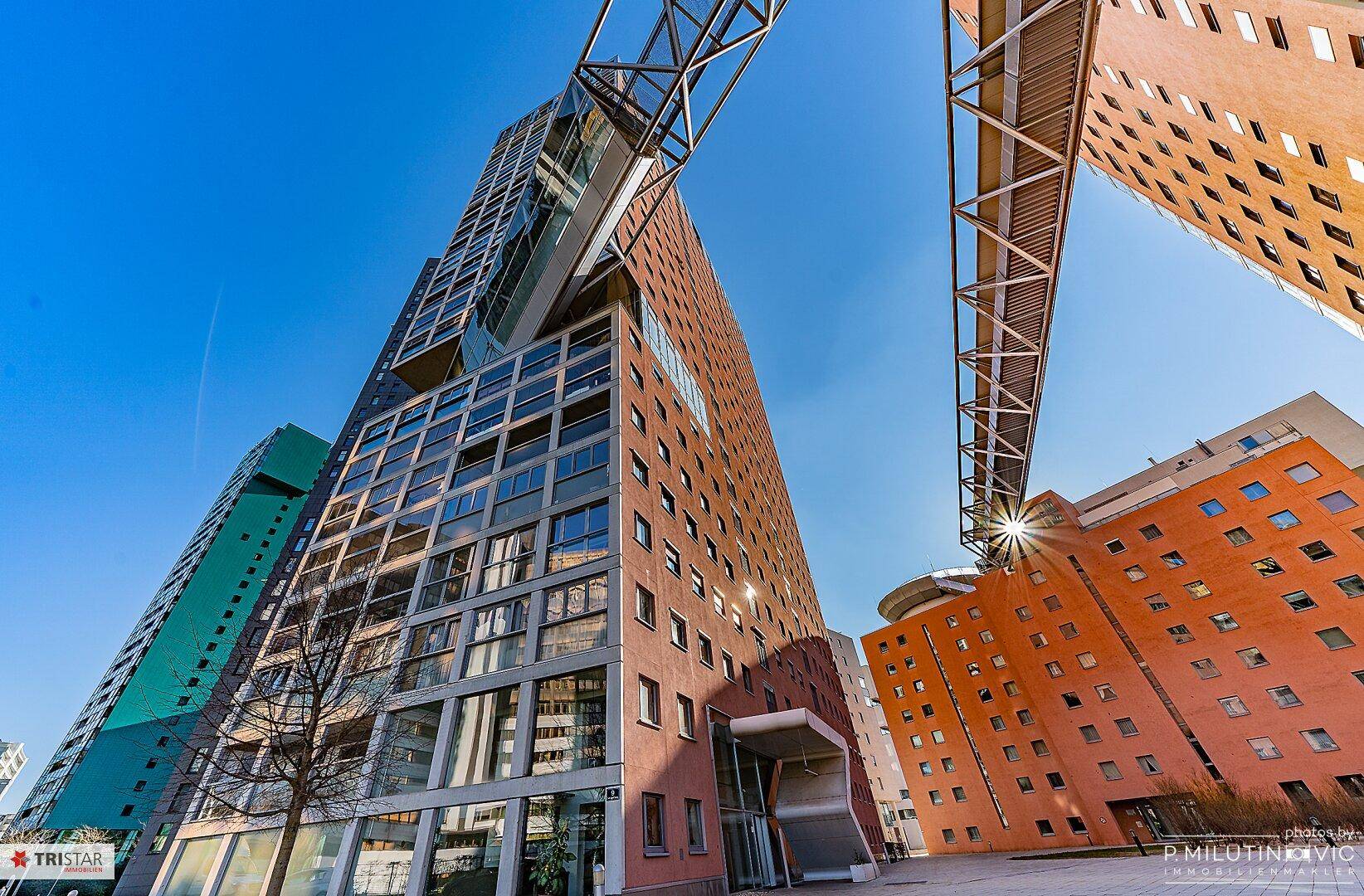 Moderne Architektur mit hohen Gebäuden und einer markanten Verbindungsbrücke unter blauem Himmel.