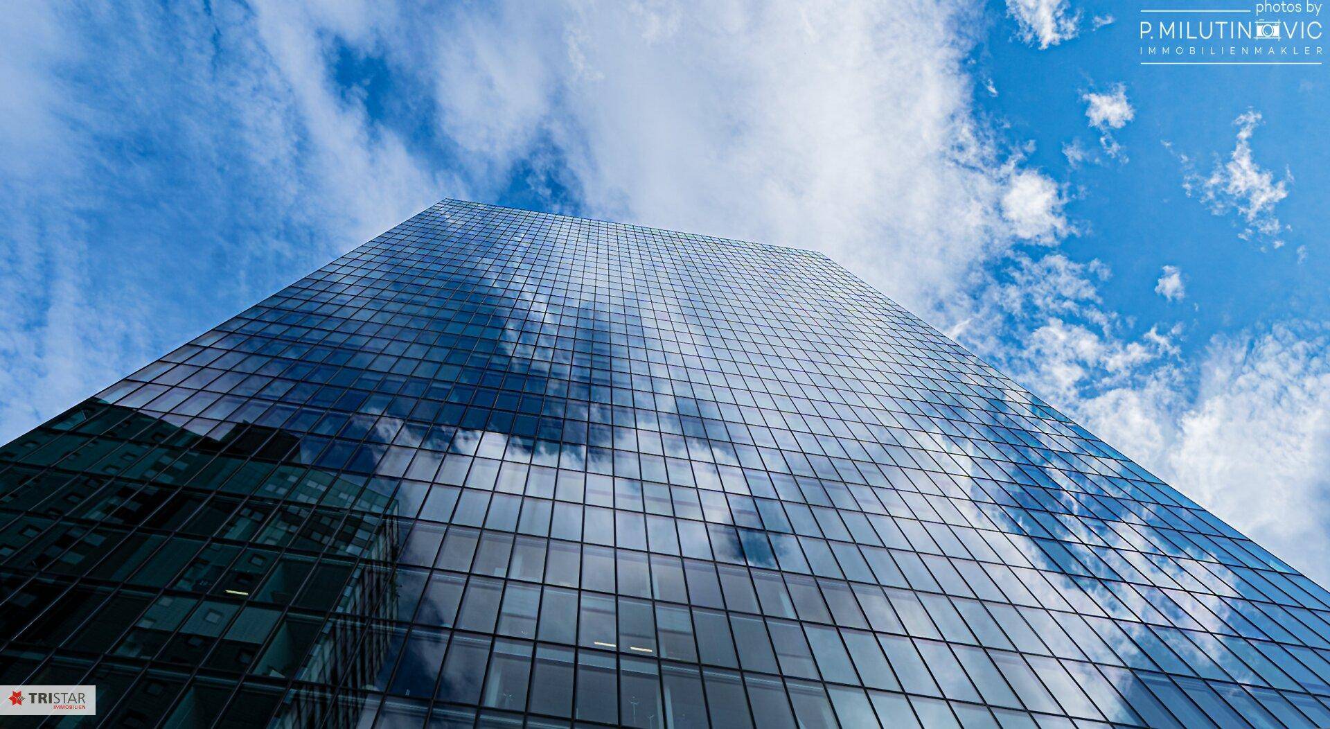 Hohes Gebäude mit spiegelnder Glasfassade unter einem klaren blauen Himmel.