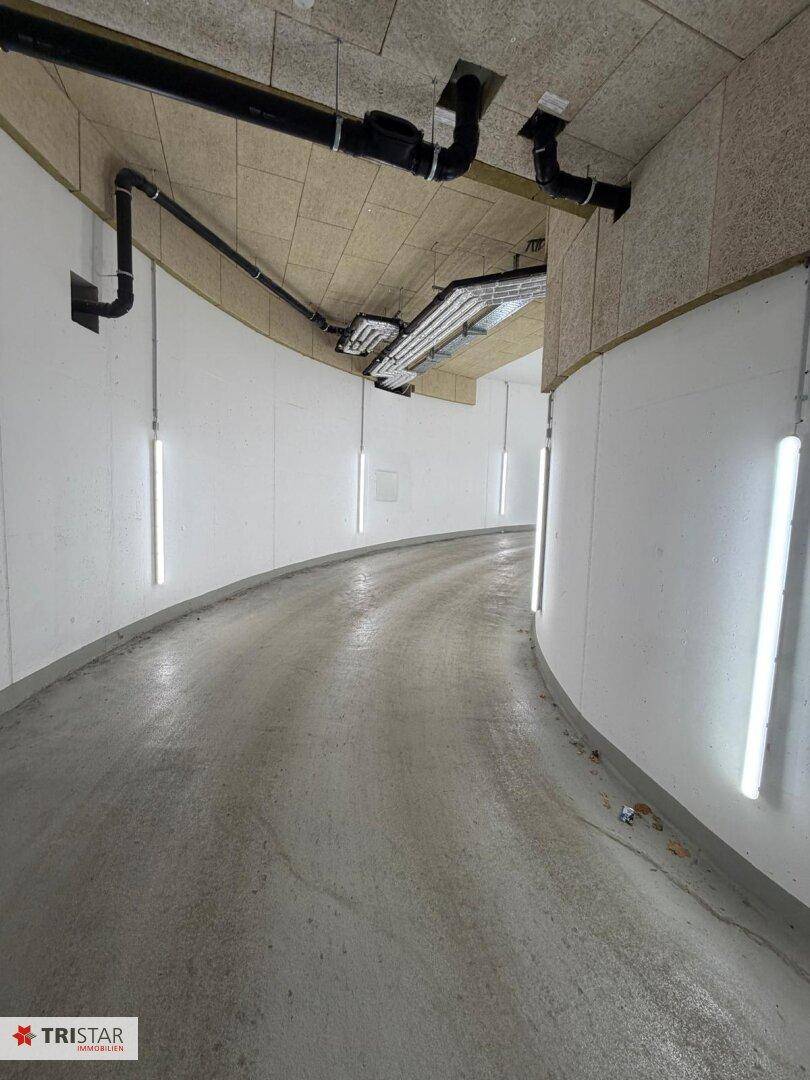 Geschwungene Zufahrtsrampe zu einer Tiefgarage mit hellen Wänden und moderner Beleuchtung.