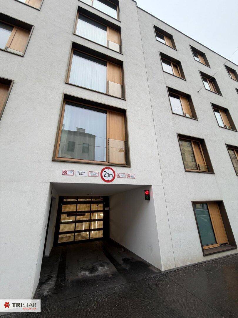 Moderne Gebäudefassade mit zahlreichen Fenstern und der Einfahrt zur Tiefgarage.