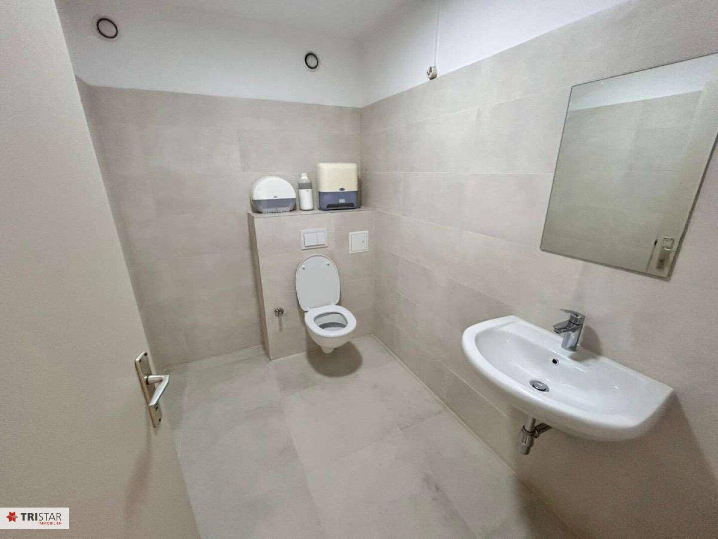 Modernes WC mit Wand-WC, Waschbecken und hellen Fliesen an Wänden und Boden.