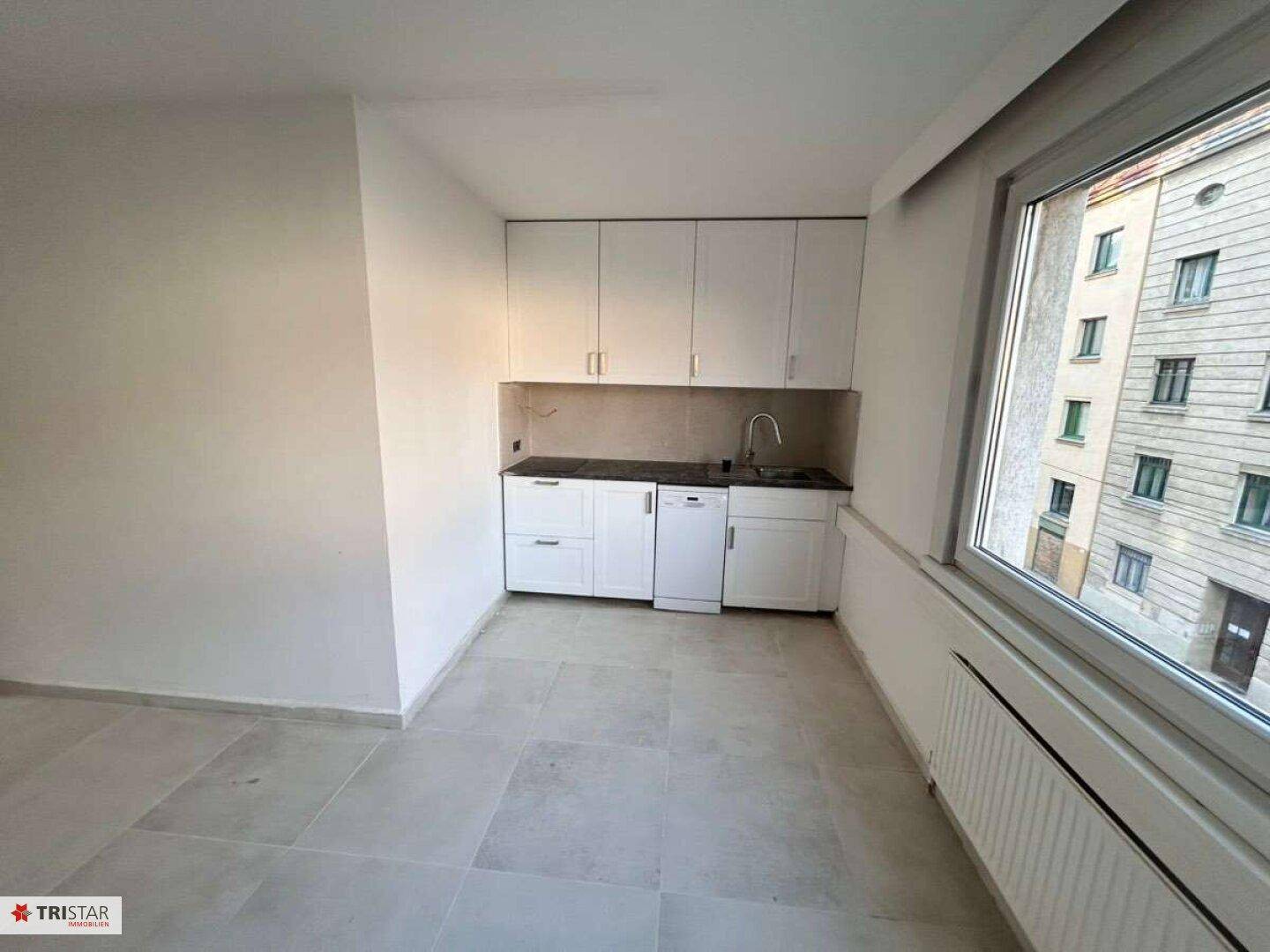 Funktionale Küchenzeile mit weißen Schränken und Fliesenboden in einem hellen Raum mit Fenster.