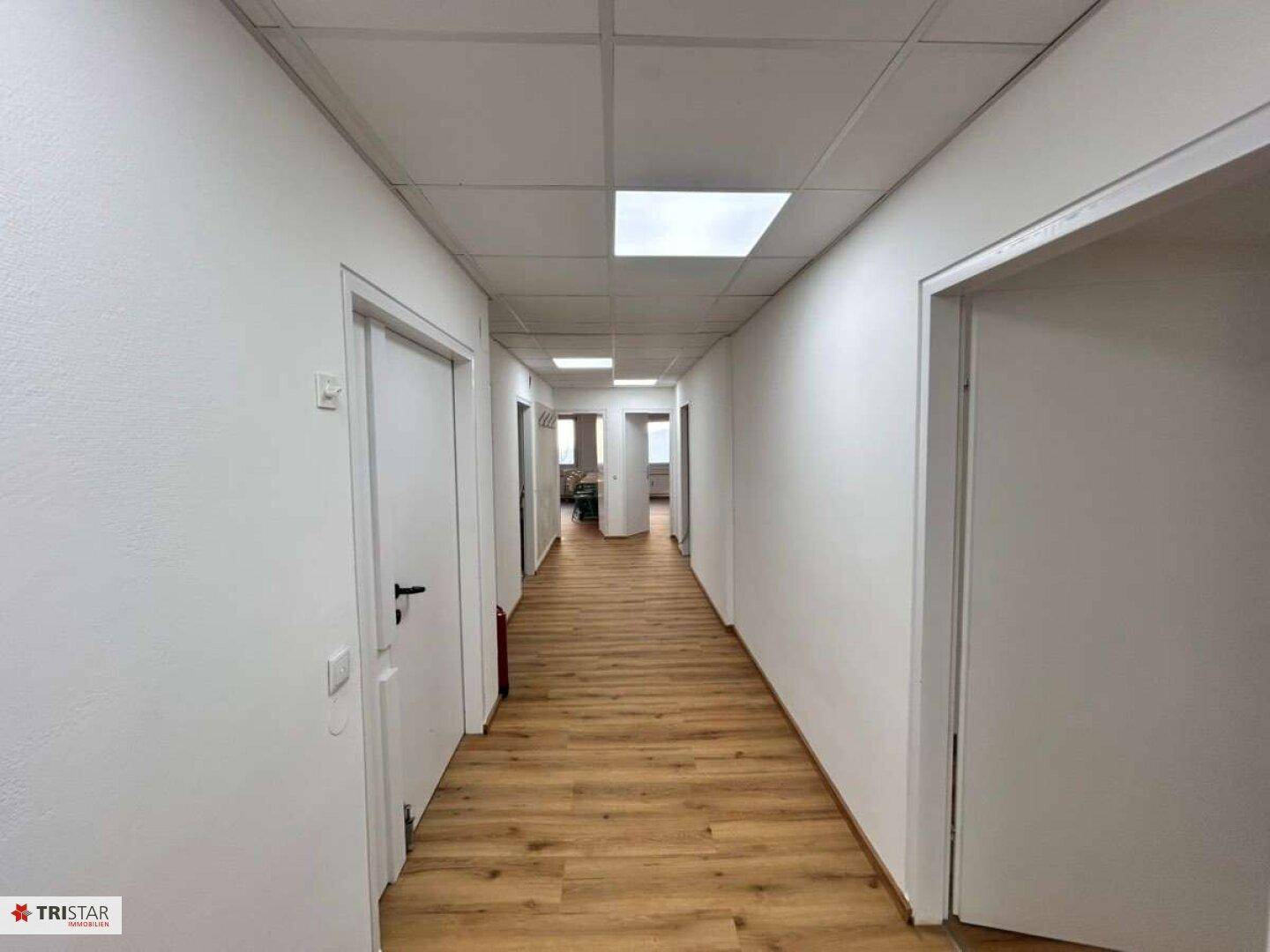 Langer, heller Flur mit Laminatboden und vielen Türen, der zu den verschiedenen Büroeinheiten führt.