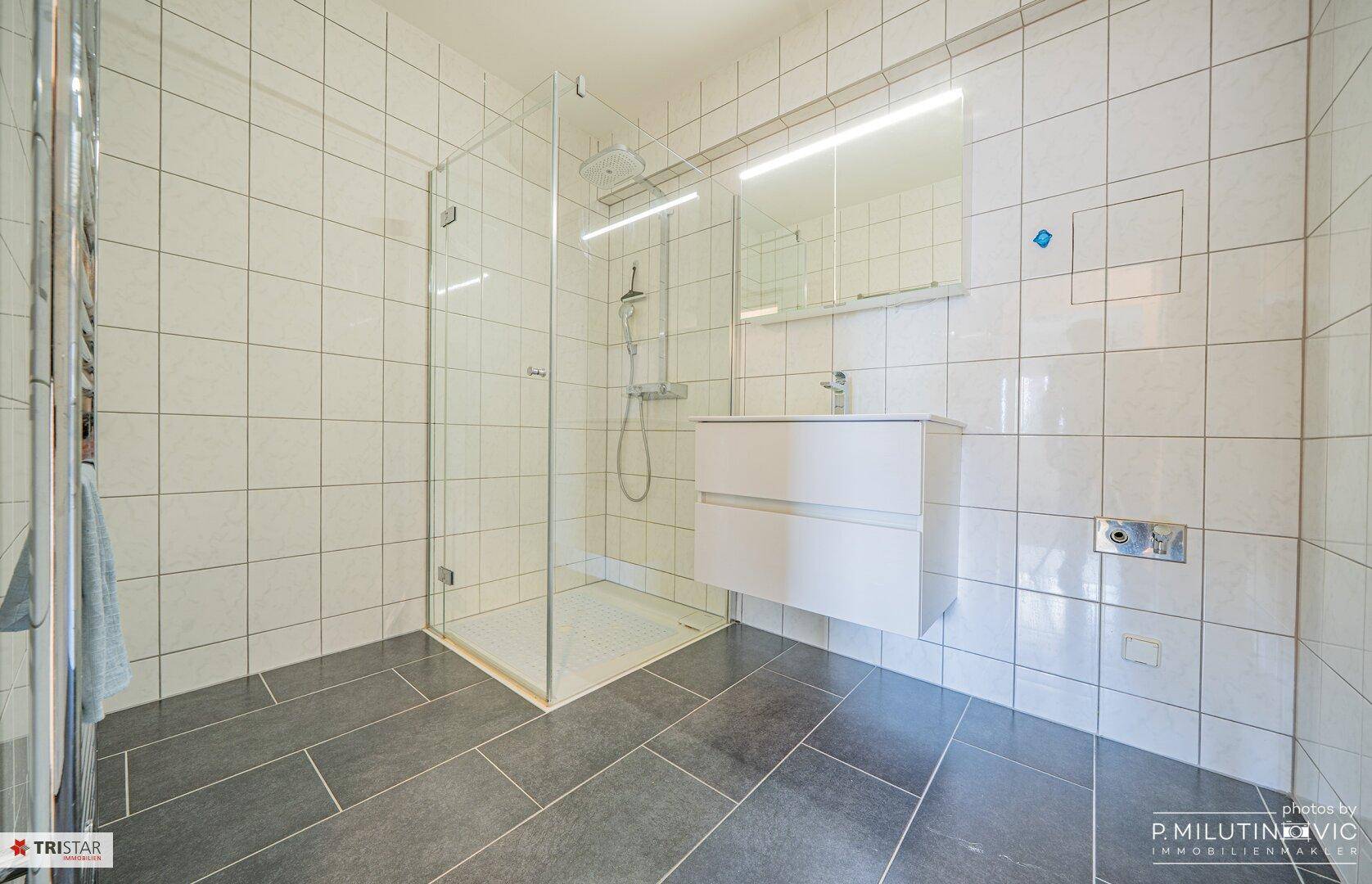 Helles Badezimmer mit großer Duschkabine, modernem Waschtisch und weißen Fliesen.
