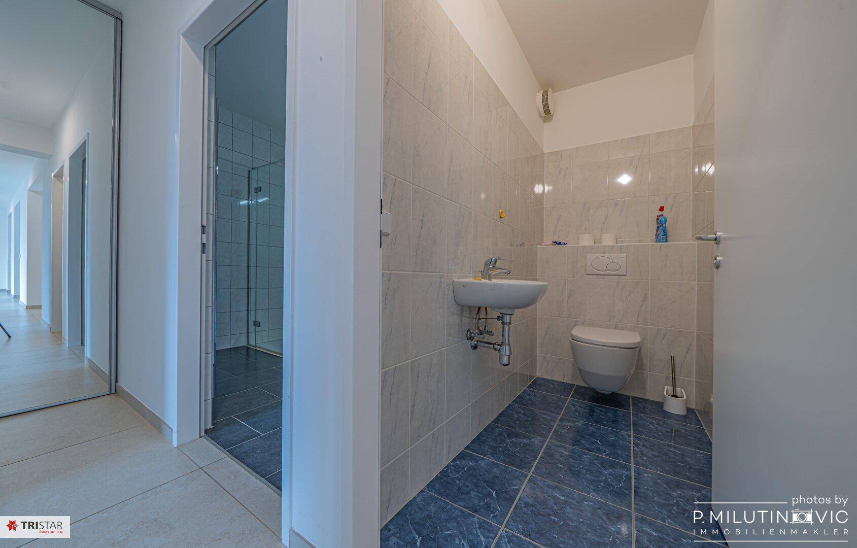 Separate Gästetoilette mit Waschbecken, WC und blauen Bodenfliesen.