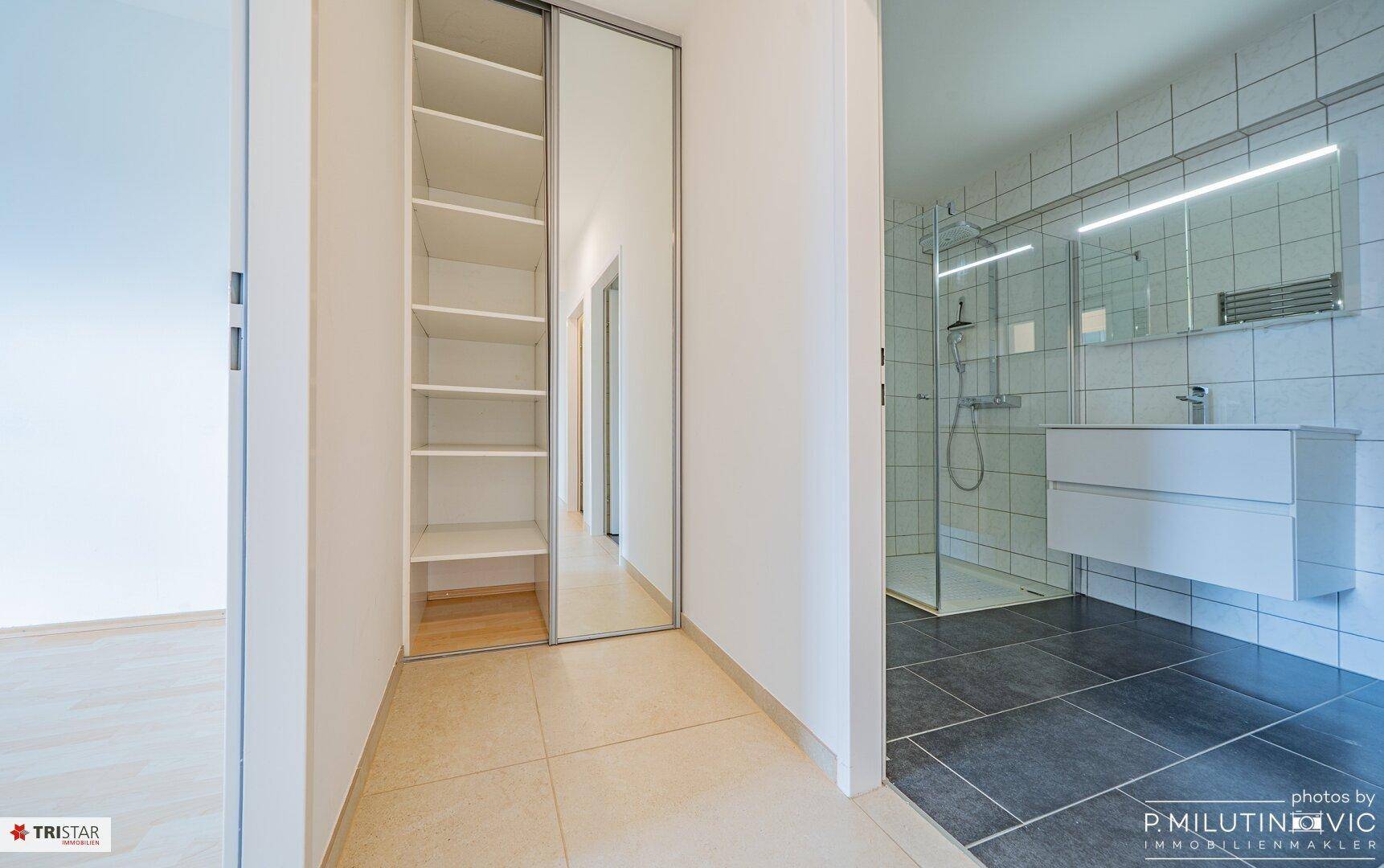 Modernes Badezimmer mit begehbarer Dusche, Waschtisch und integrierten Regalen.