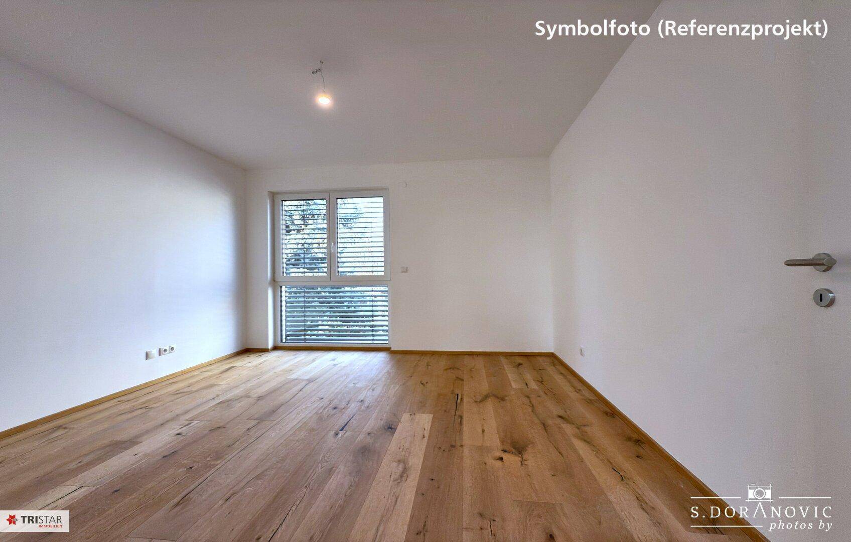 Leeres Schlafzimmer mit Holzboden und Fenster, das einen Blick ins Grüne bietet.