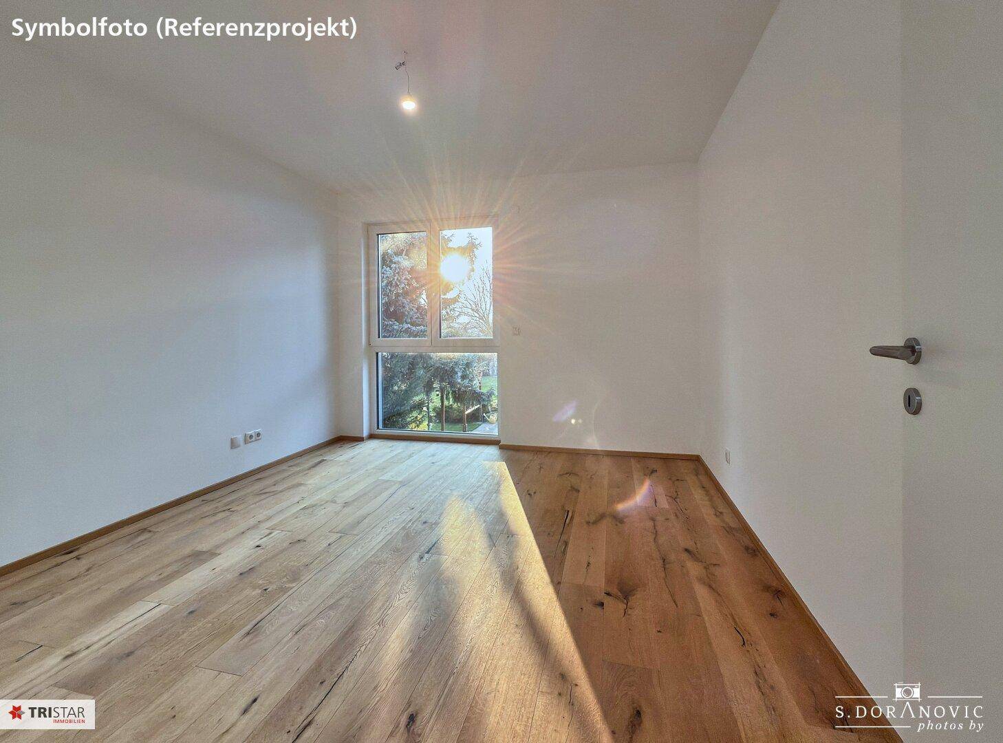 Sonniges Zimmer mit Holzboden und großen Fenstern, die viel natürliches Licht hereinlassen.