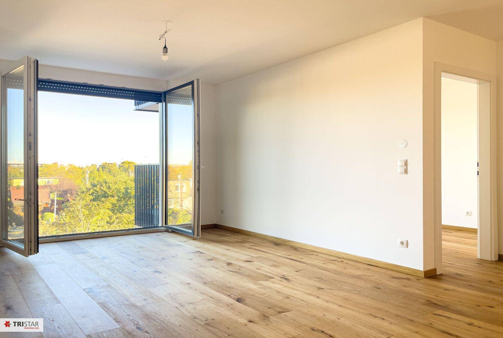 Heller, leerer Raum mit großen Fenstern und Holzboden, ideal für ein Wohnzimmer.