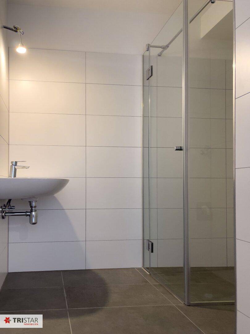 Modernes Badezimmer mit Waschbecken, Duschkabine und weißen Wandfliesen.