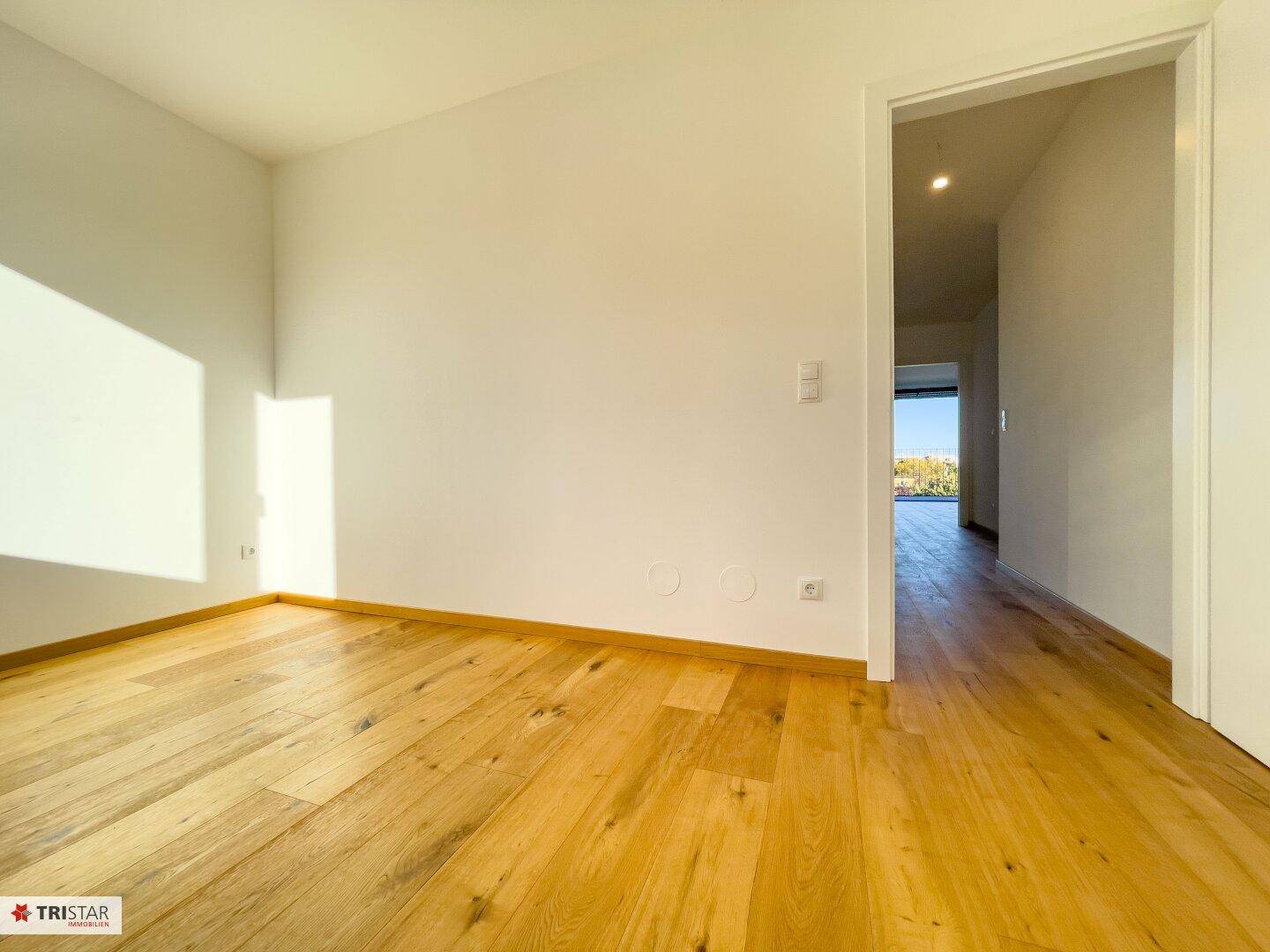 Heller, leerer Raum mit Holzboden und Türöffnung, ideal als Schlaf- oder Arbeitszimmer.