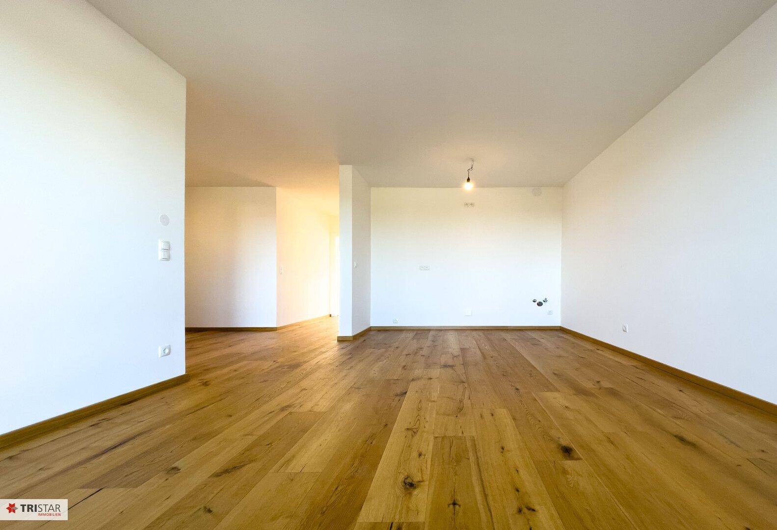 Geräumiger, leerer Wohnbereich mit Holzboden und viel natürlichem Licht.