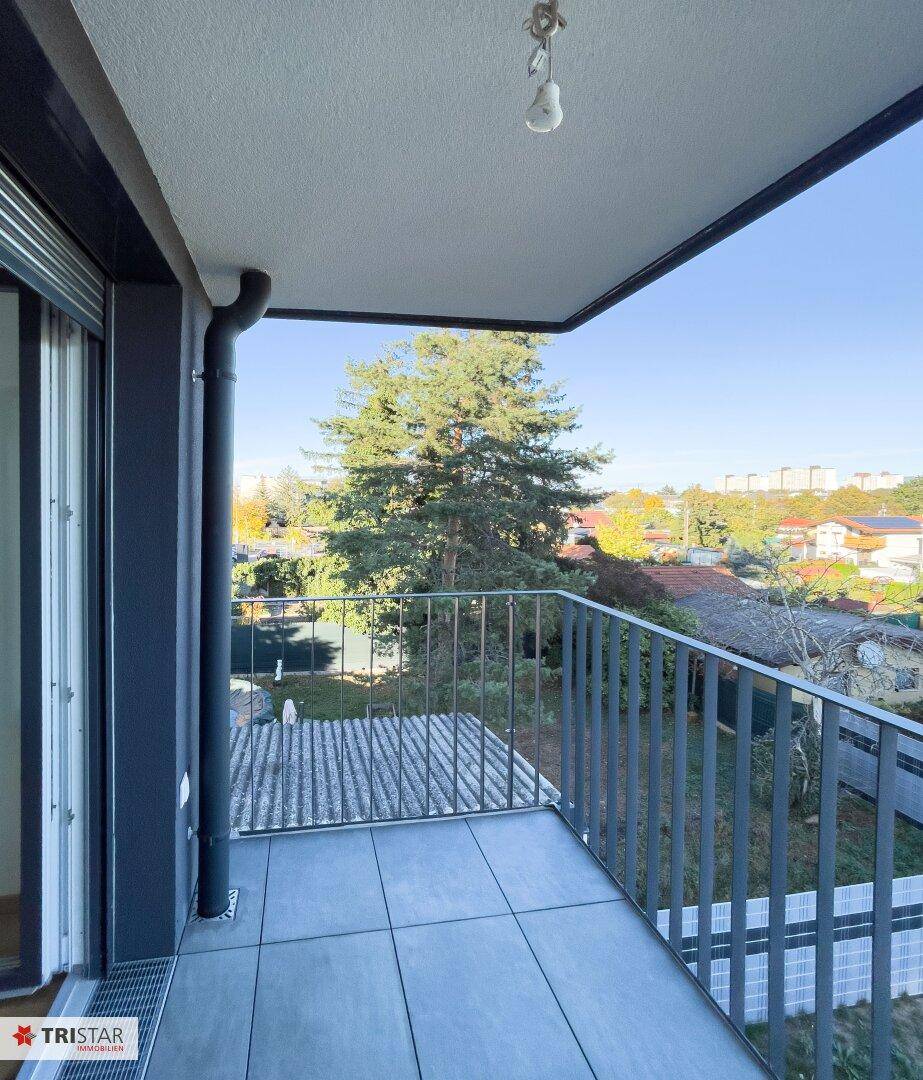Kleiner Balkon mit Fliesenboden und Blick auf Bäume und die umliegende Wohngegend.