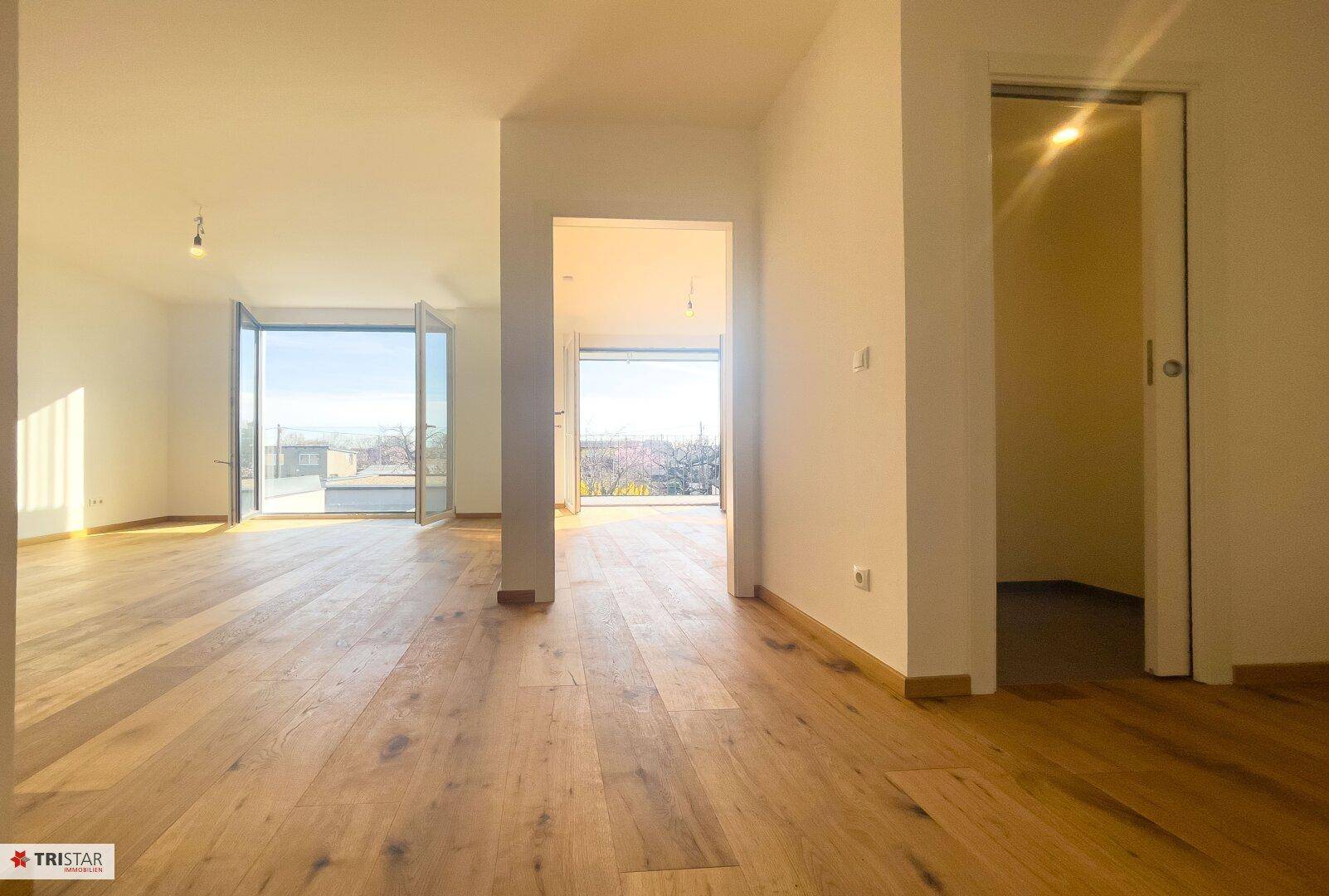 Geräumiger, offener Wohnbereich mit Holzboden und viel Tageslicht durch große Fenster.