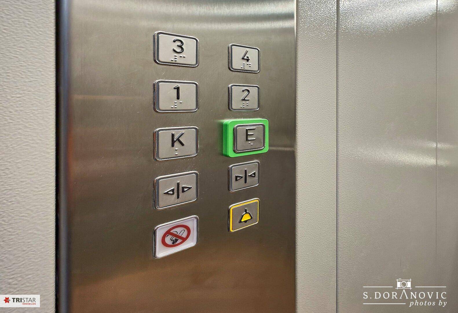 Detailaufnahme der Aufzugsknöpfe aus gebürstetem Metall mit Etagenanzeige und Notruffunktion.