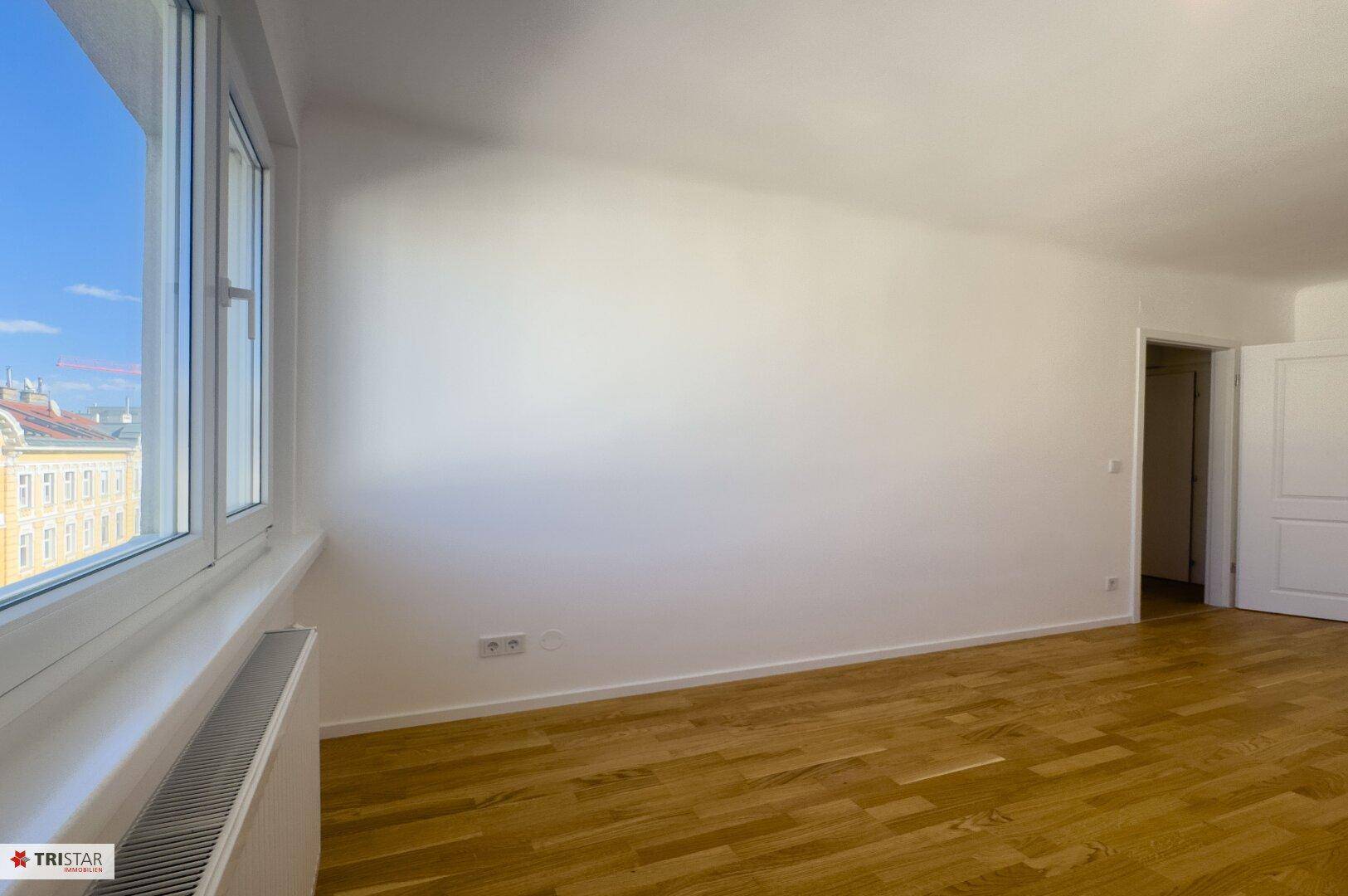 Geräumiger, heller Wohnraum mit elegantem Parkettboden und einem großen Fenster für optimale Belichtung.
