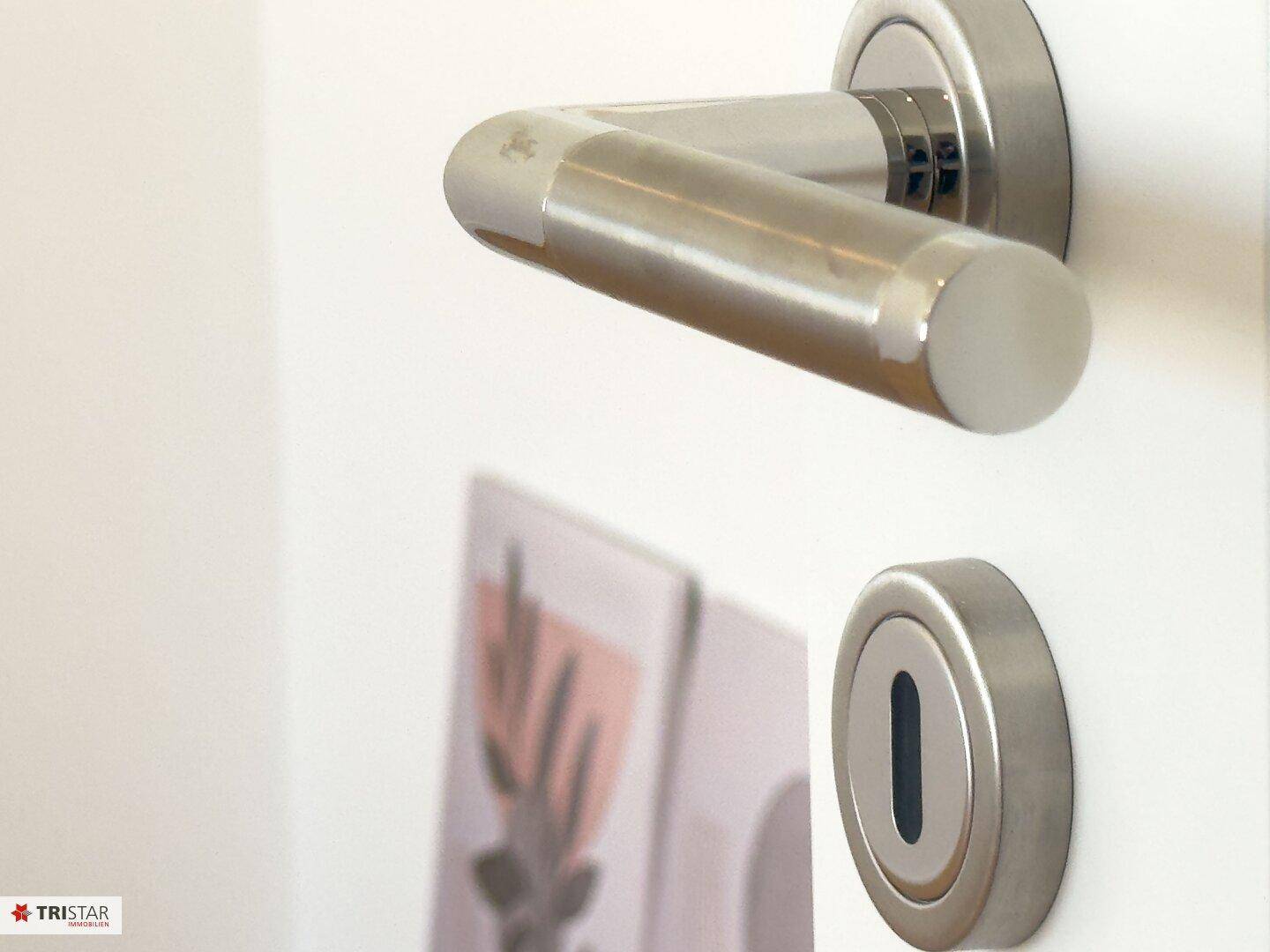 Detailaufnahme eines modernen Türgriffs aus gebürstetem Metall an einer weißen Innentür.