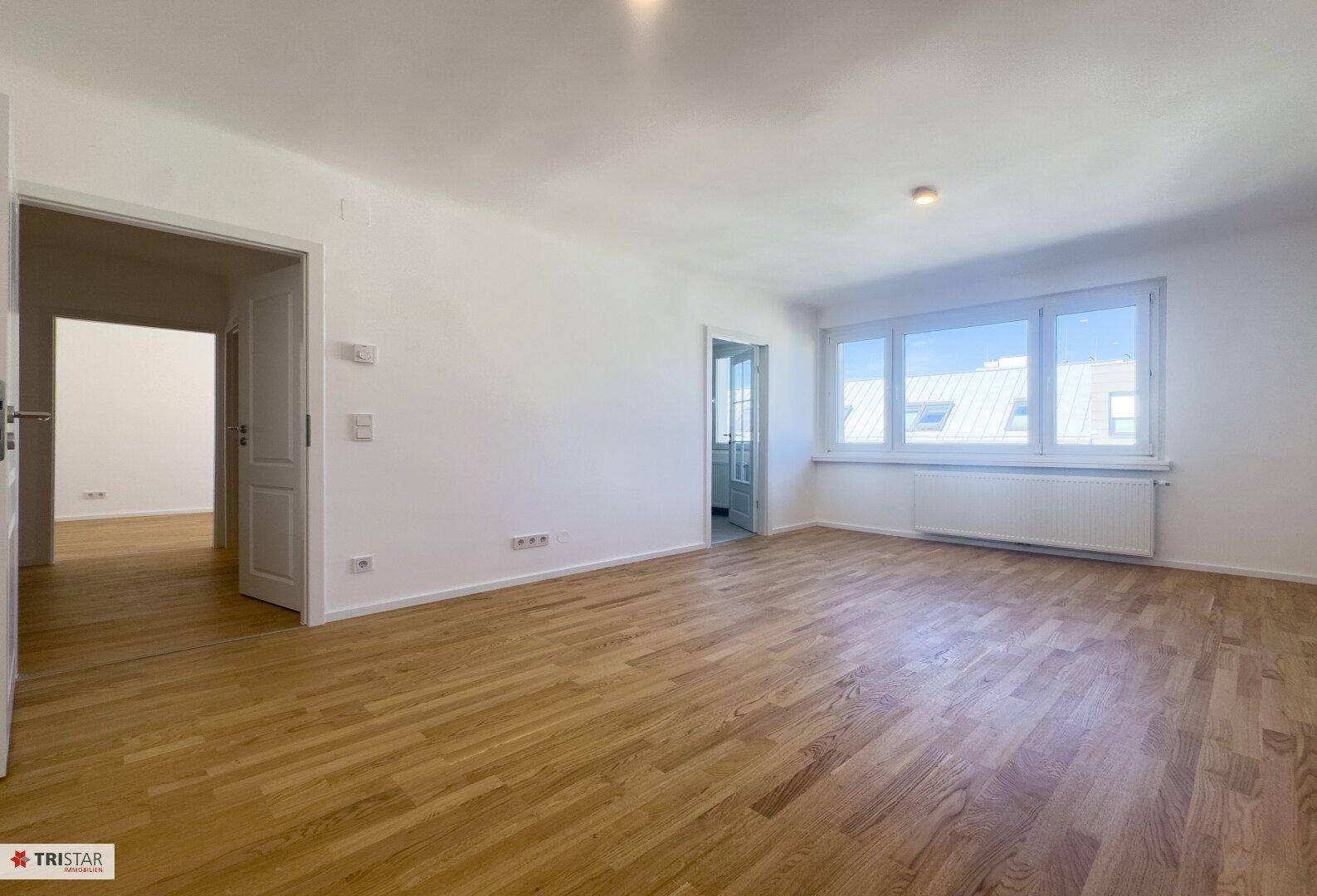 Großzügiger, heller Wohnraum mit elegantem Parkettboden und weitem Blick durch die Fenster.
