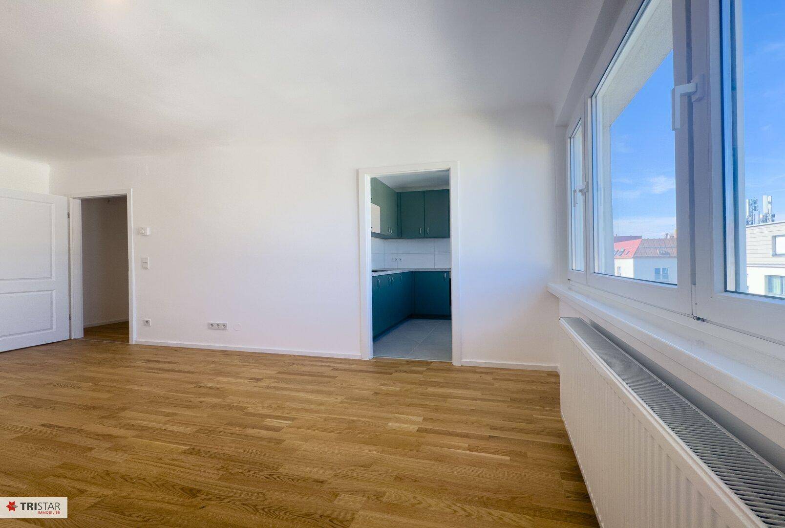Heller Wohnraum mit Parkettboden und Blick in die separate Küche mit modernen Schränken.