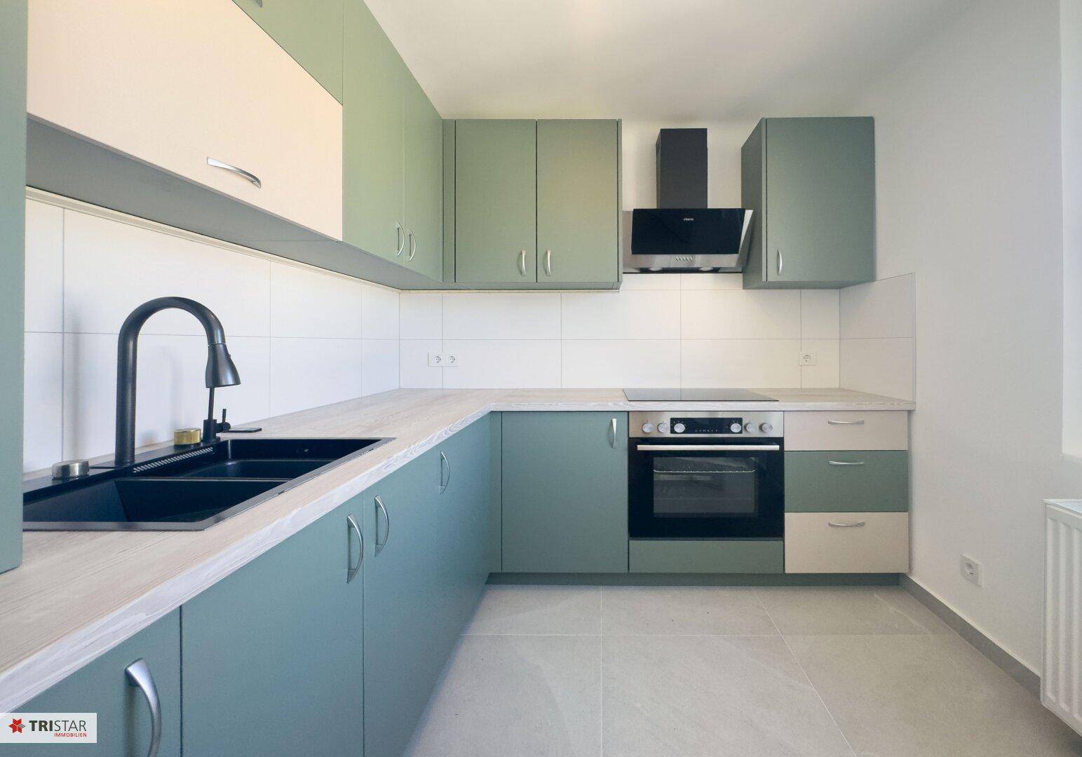 Moderne Einbauküche mit hellgrünen und beigen Fronten, ausgestattet mit Herd, Backofen und Dunstabzugshaube.