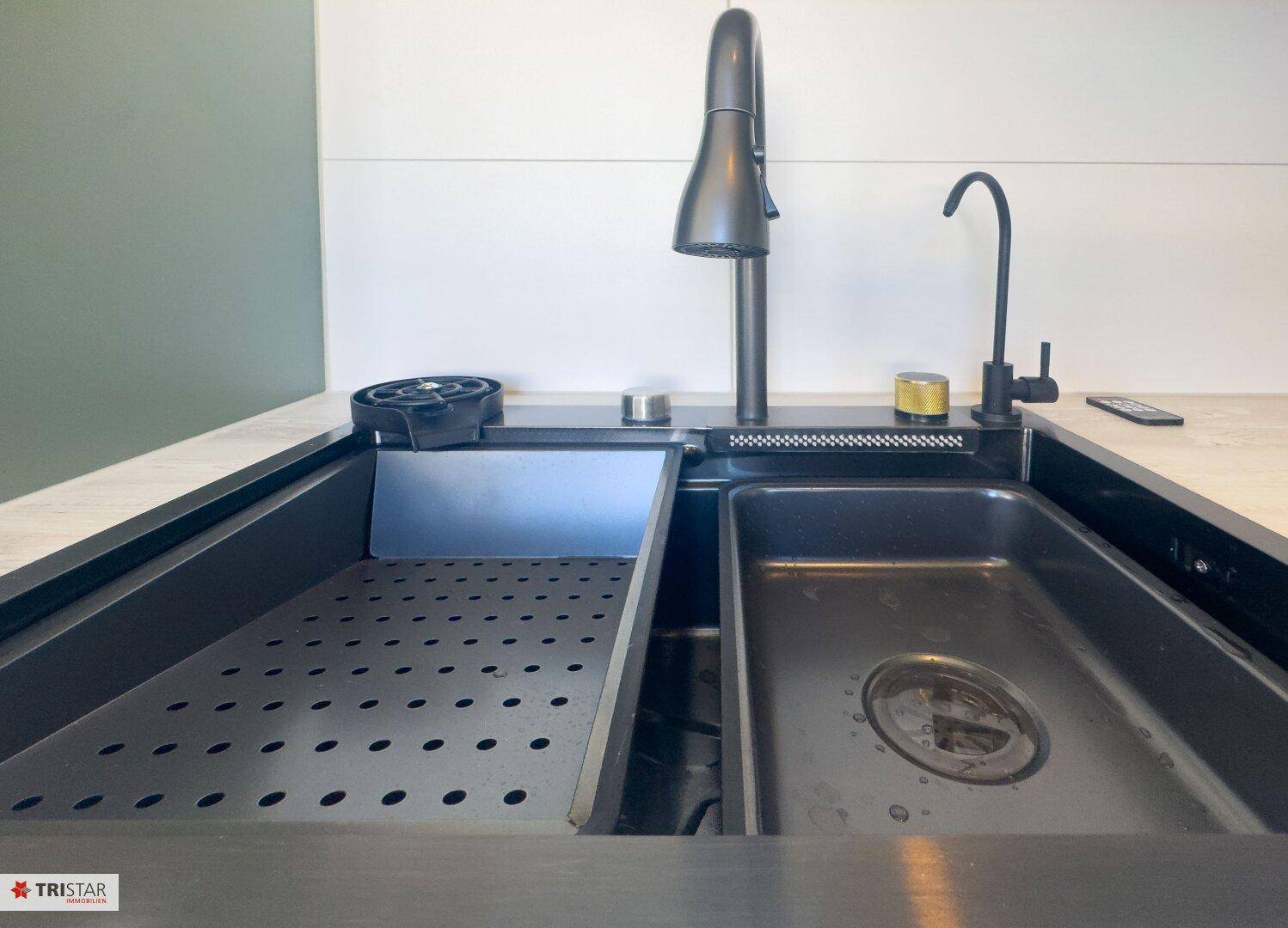 Detailaufnahme einer modernen Küchenspüle mit schwarzem Wasserhahn und integrierter Abtropffläche.
