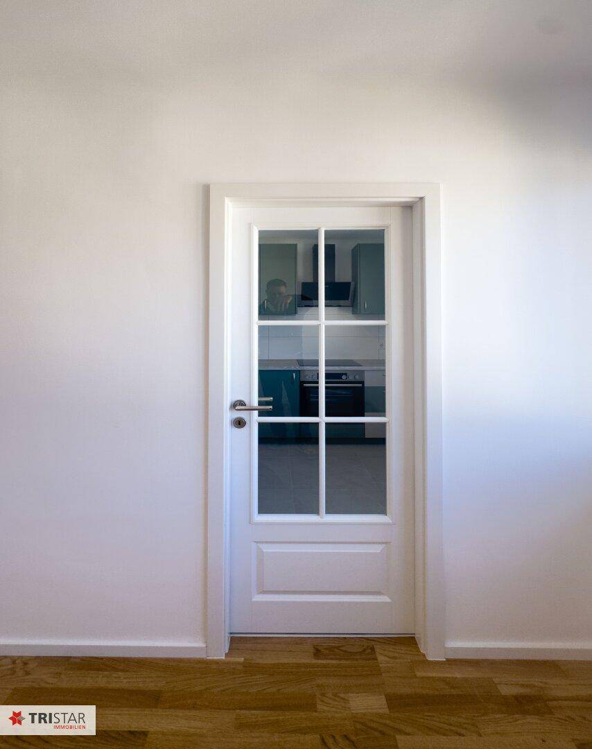 Weiße Tür mit Glaseinsätzen, die einen Blick in die moderne Küche freigibt.