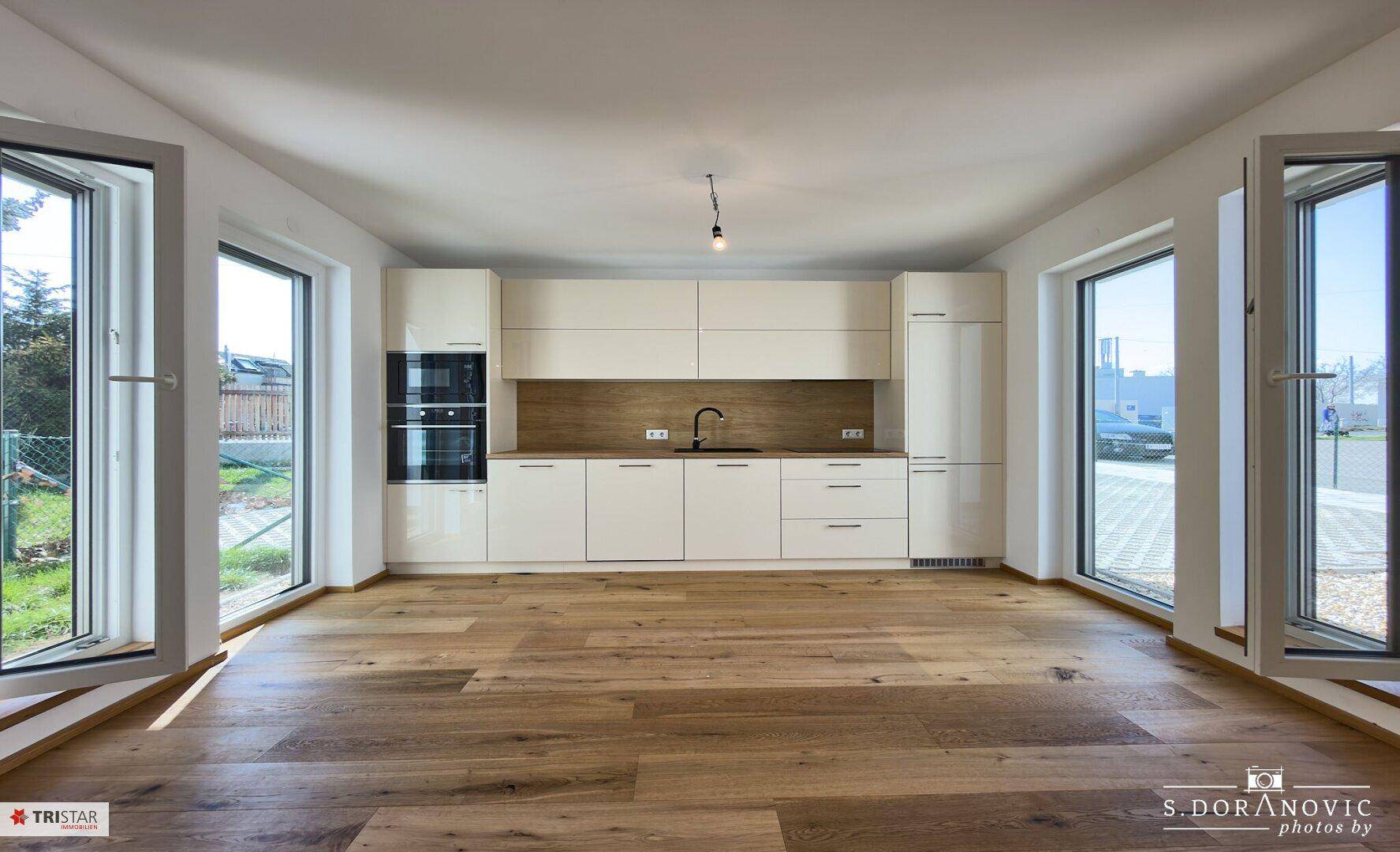 Moderne Küche mit weißen Hochglanzfronten, Holzakzenten und großen Fenstern.