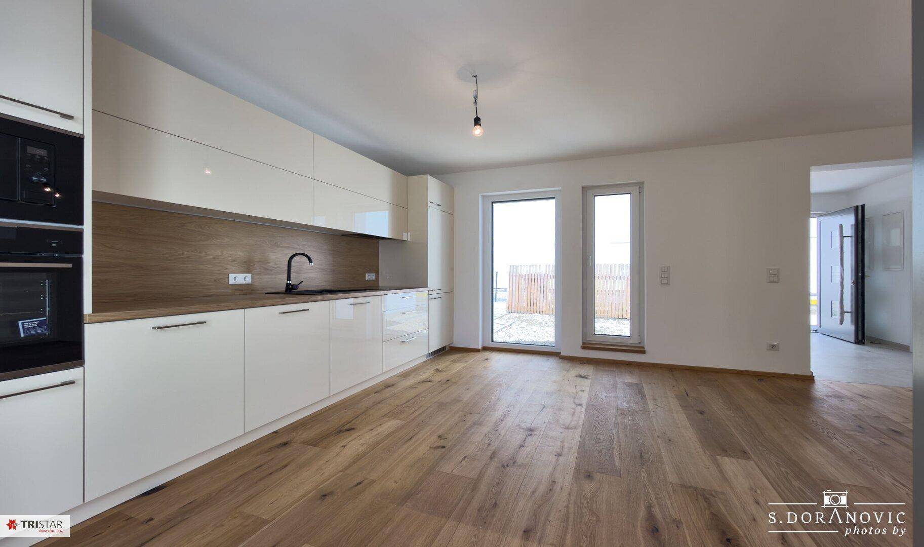 Moderne Einbauküche mit weißen Fronten, Holzakzenten und Zugang zum Außenbereich.