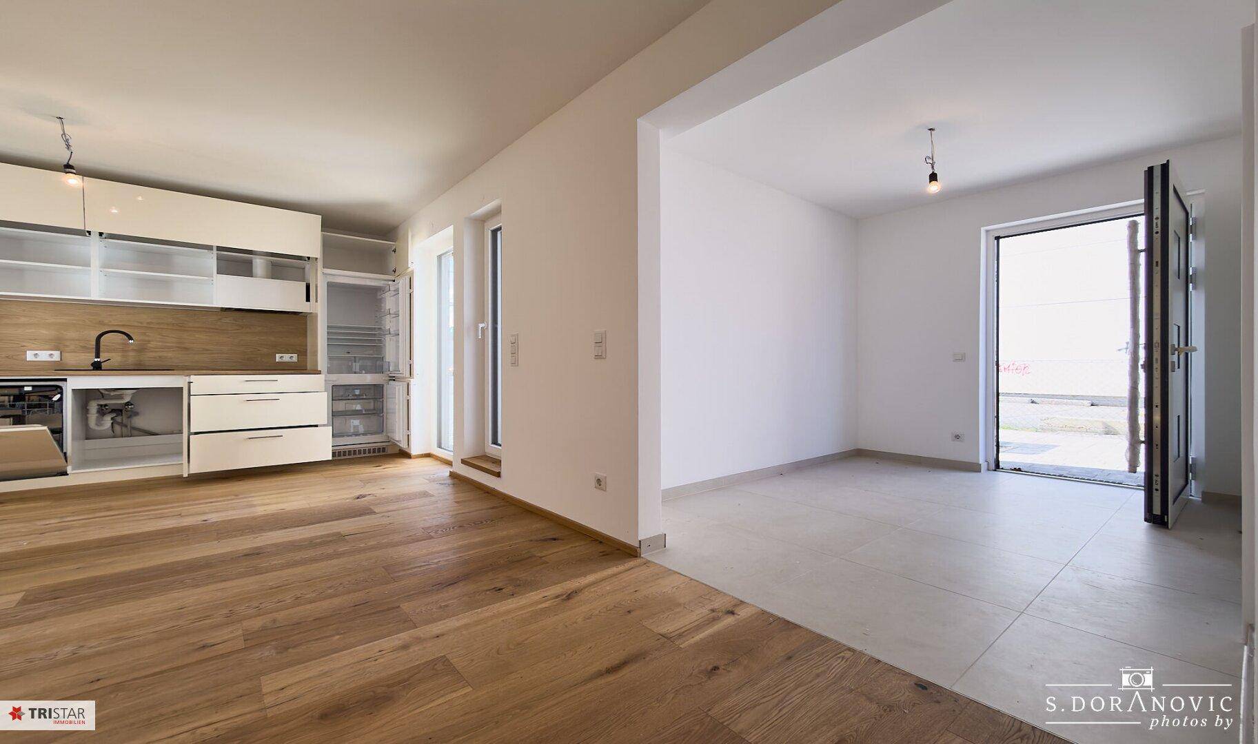 Offener Wohnbereich mit teilweise installierter Küche, Holzboden und Zugang zur Terrasse.