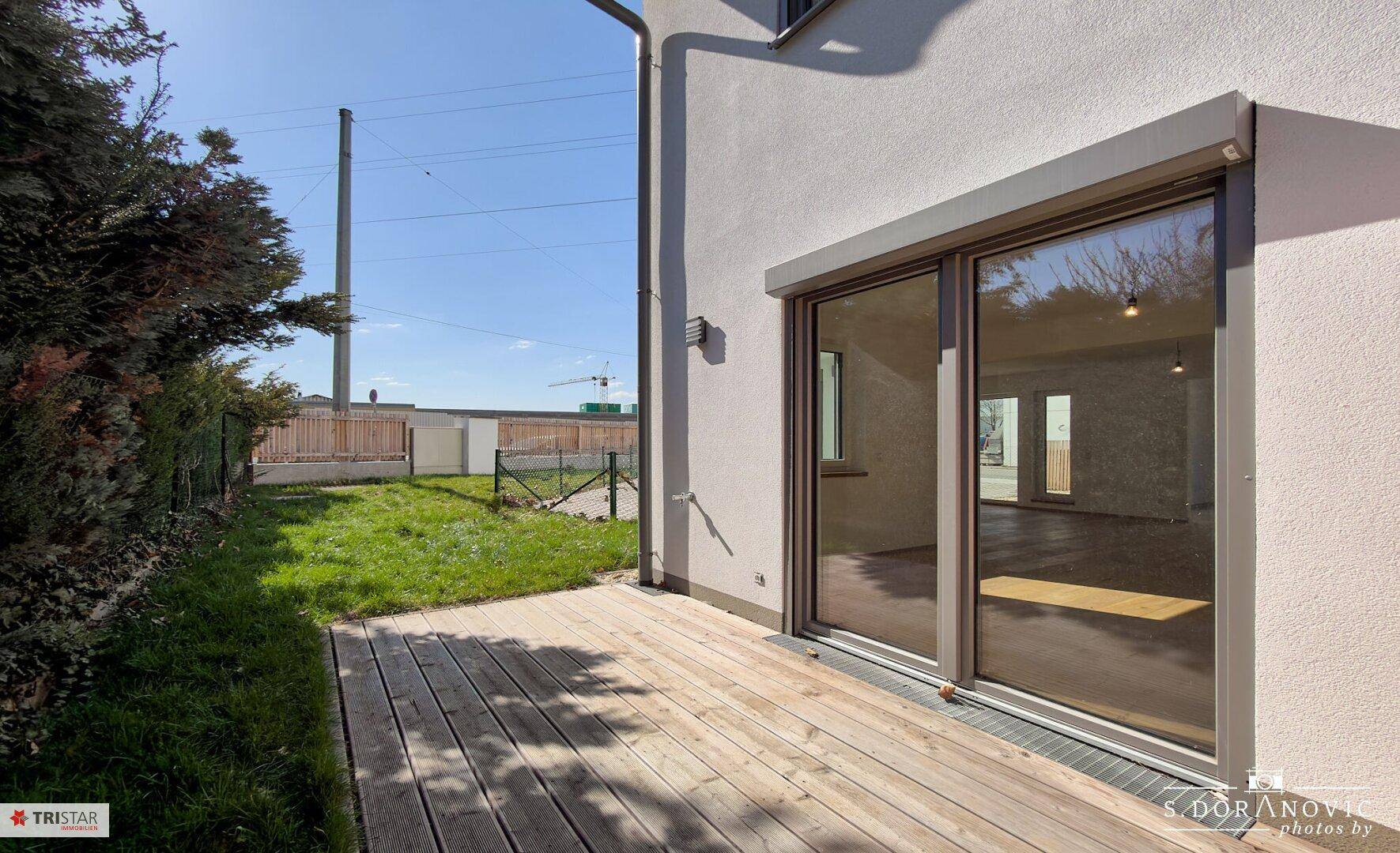 Holzterrasse am Haus mit Zugang zum Garten und Blick ins Grüne.