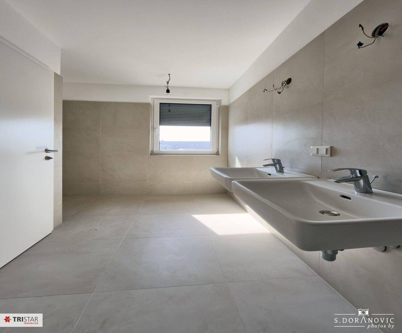 Helles Badezimmer mit zwei Waschbecken, Fenster und modernen Fliesen.