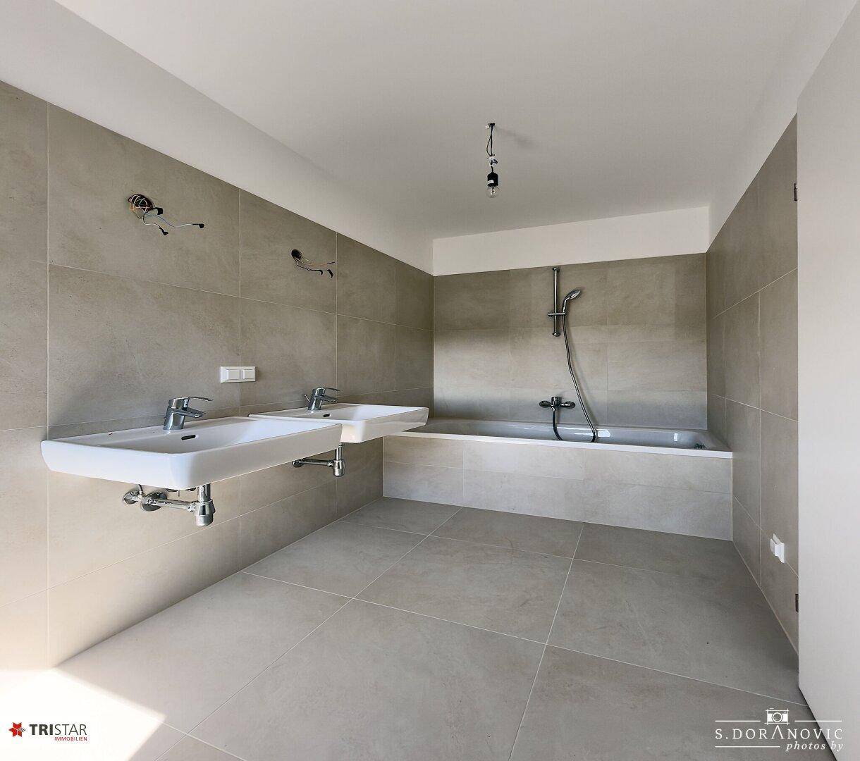Modernes Badezimmer mit zwei Waschbecken, Badewanne und hellgrauen Fliesen.